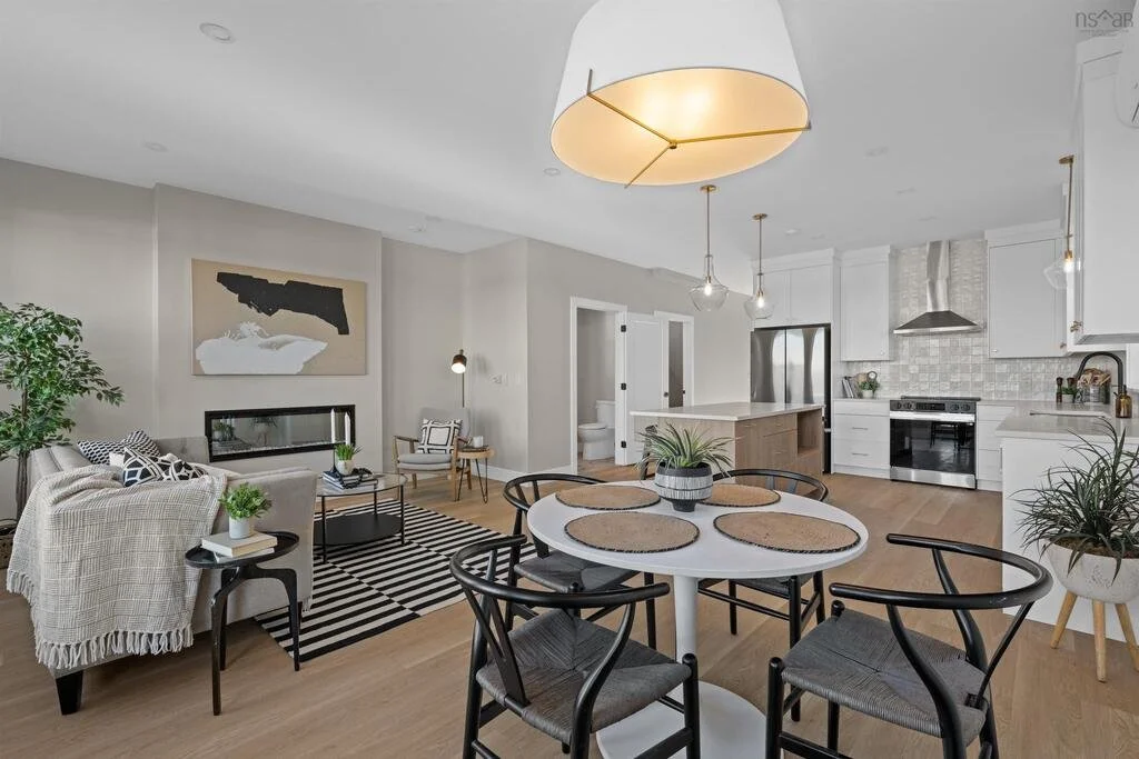 Modern open-plan living area with a dining table, living room, and kitchen, featuring neutral colors, wooden floors, plants, and stylish lighting fixtures.