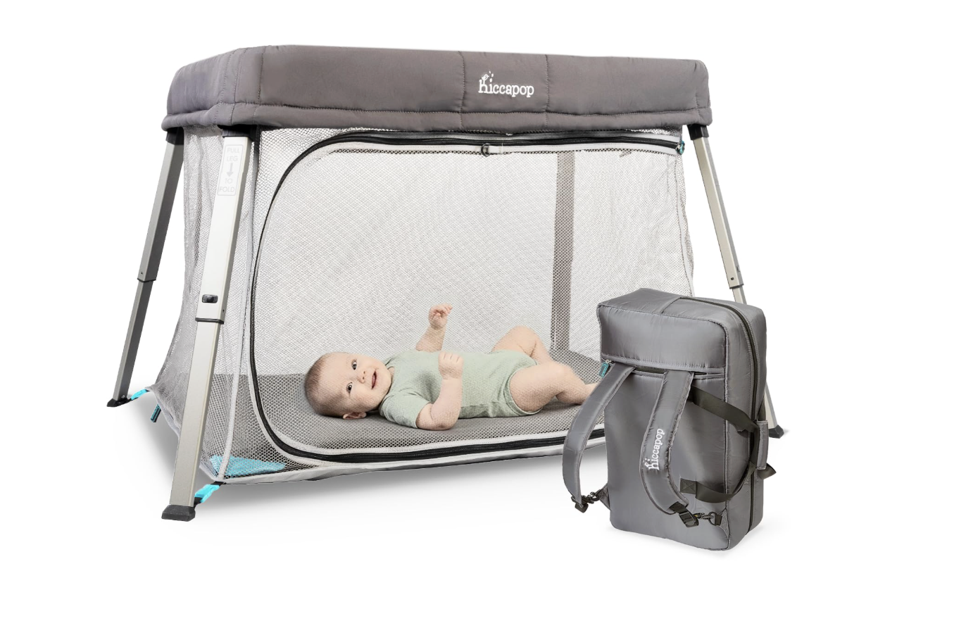 Baby in green onesie lays in a mesh and grey pack and play