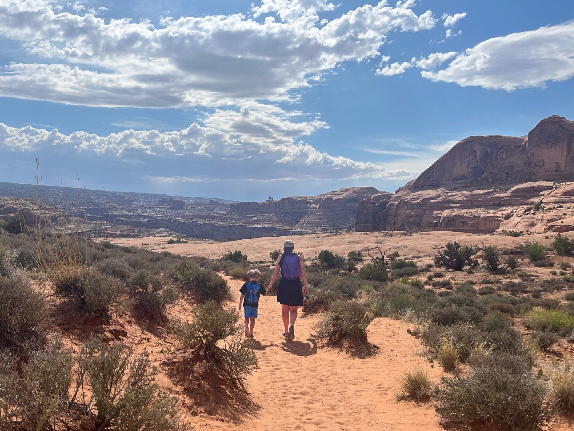 The author and her son hiking while holding hands on the Corona Arch trail in Moab, Utah