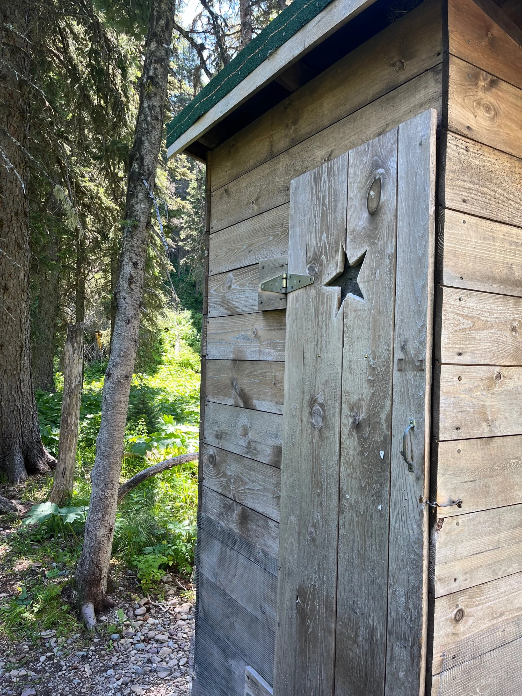 Wooden outhouse with a star carved in the door on the Grinnell Lake Trail