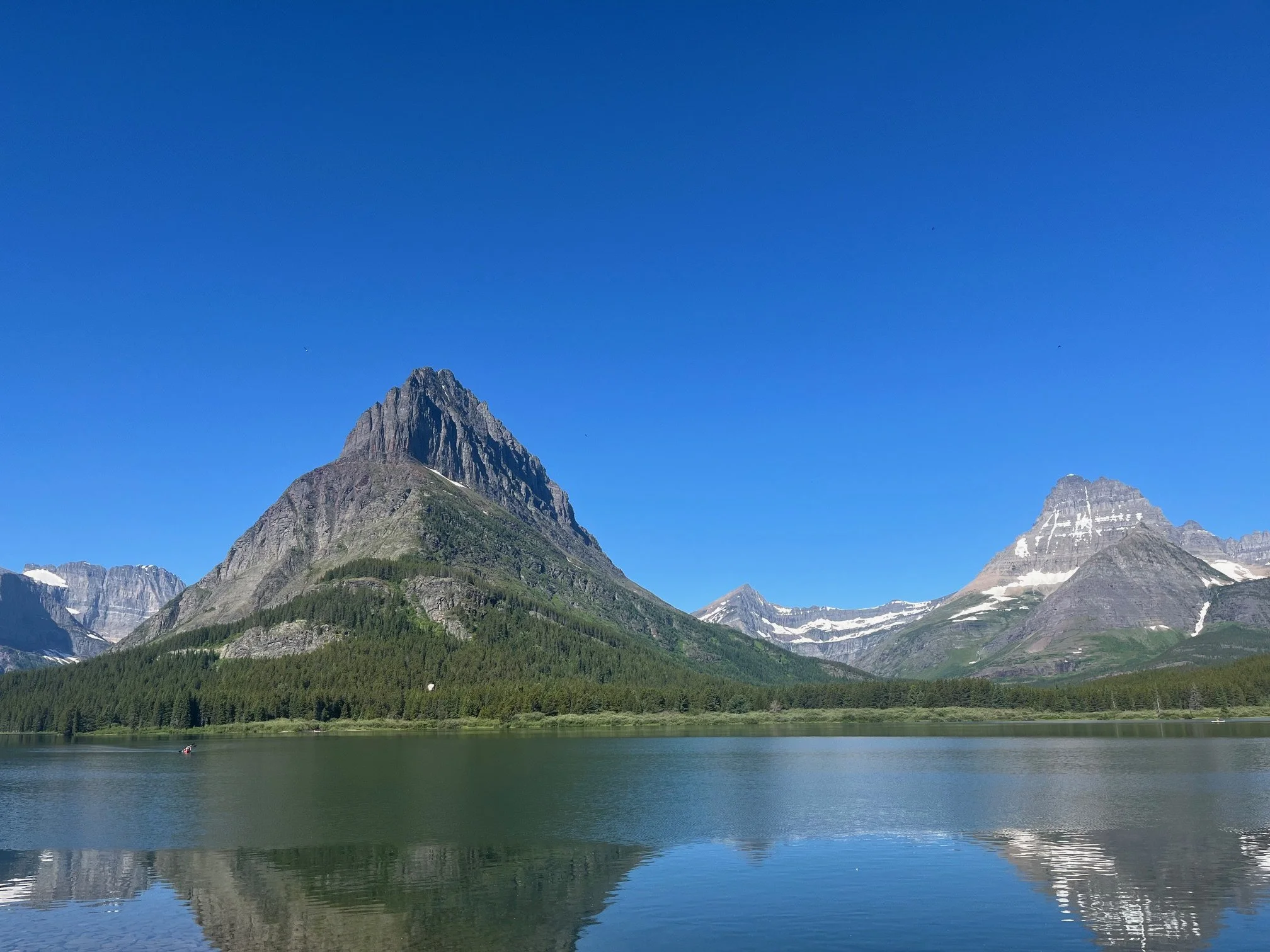 Swiftcurrent Lake with large snow covered mountains behind it