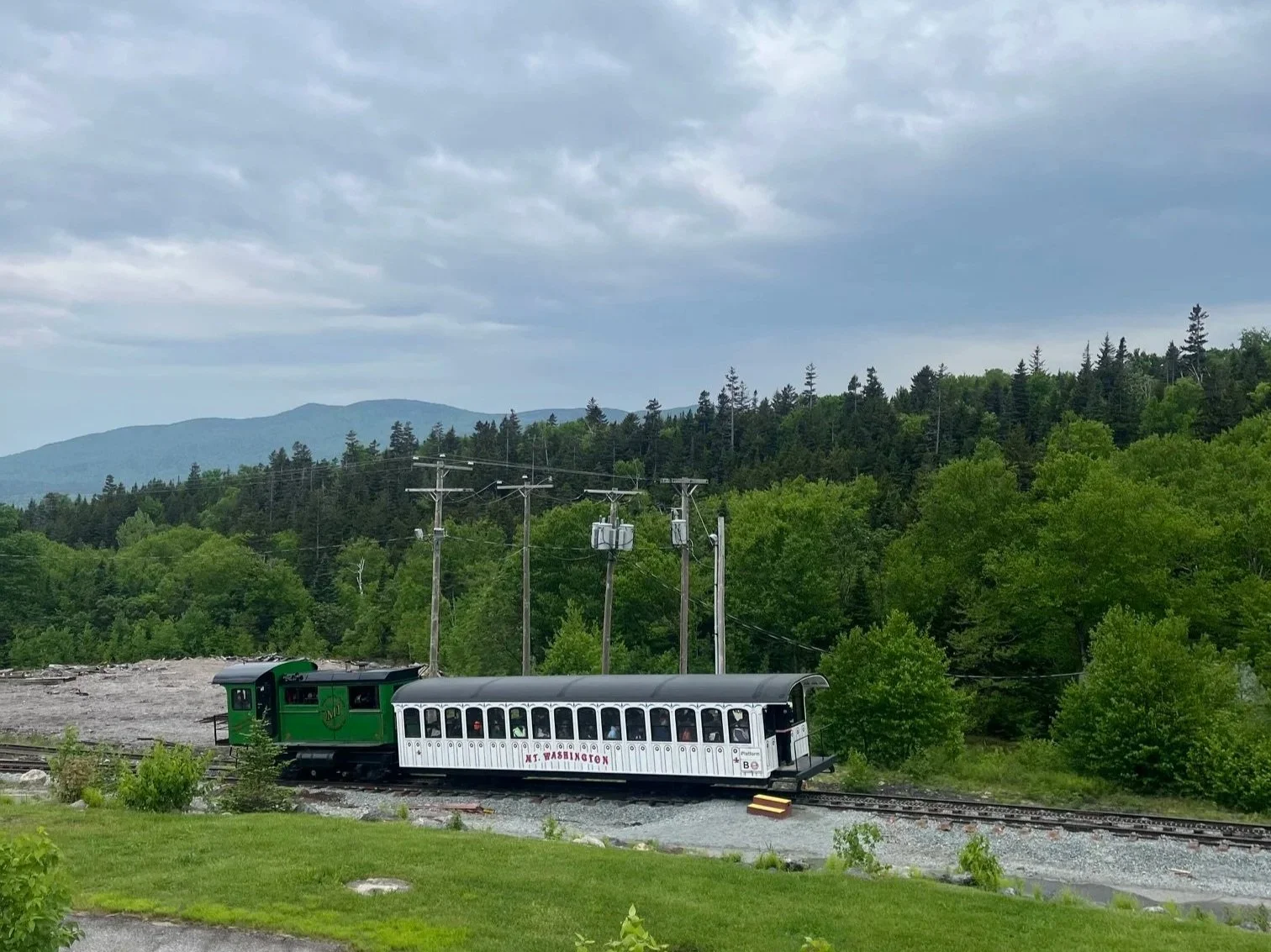 Green locomotive and white passenger car parked on the track outside of the Mt. Washington base station