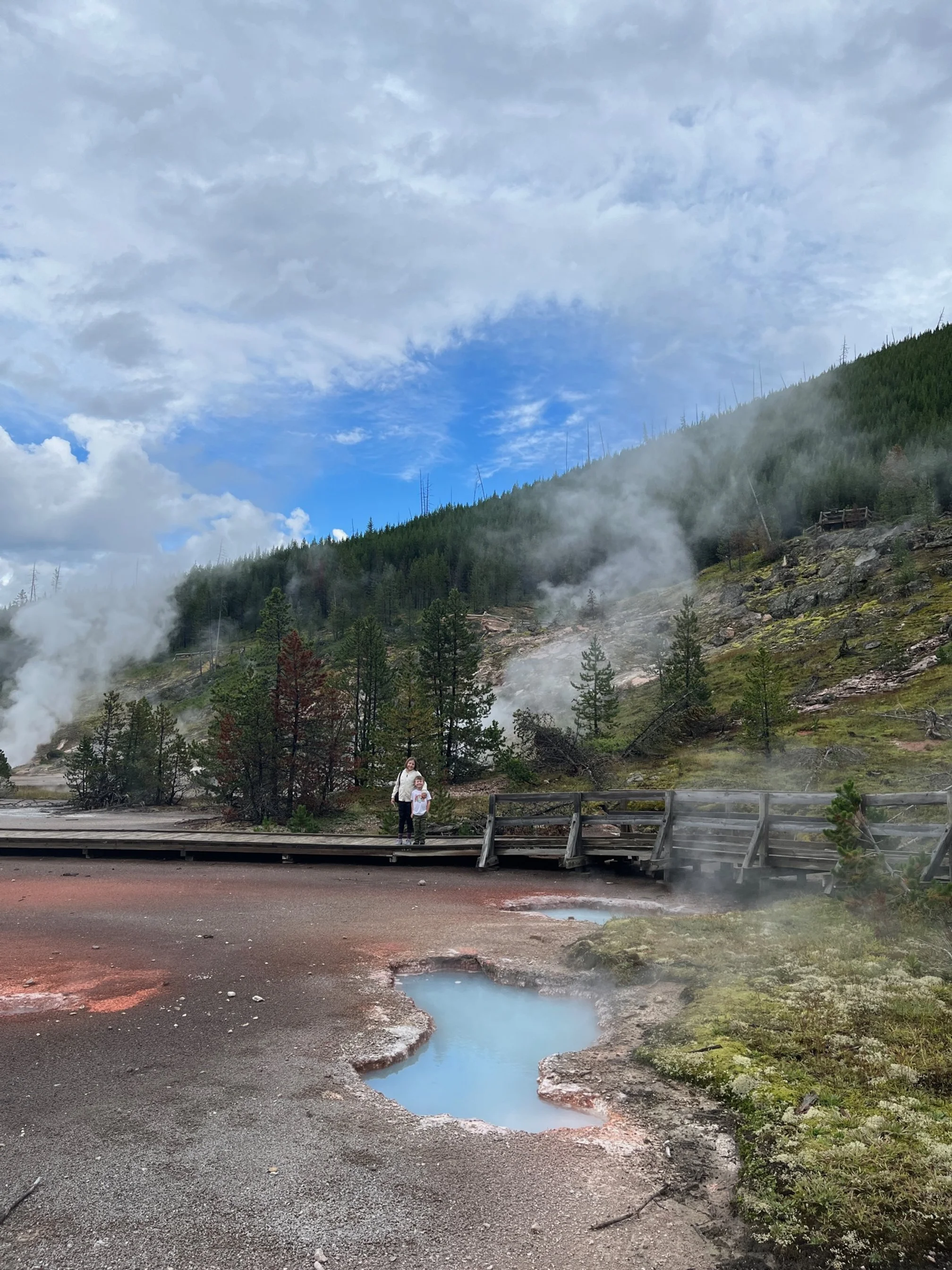 The author's children standing on a boardwalk in front of a brilliantly blue hot spring