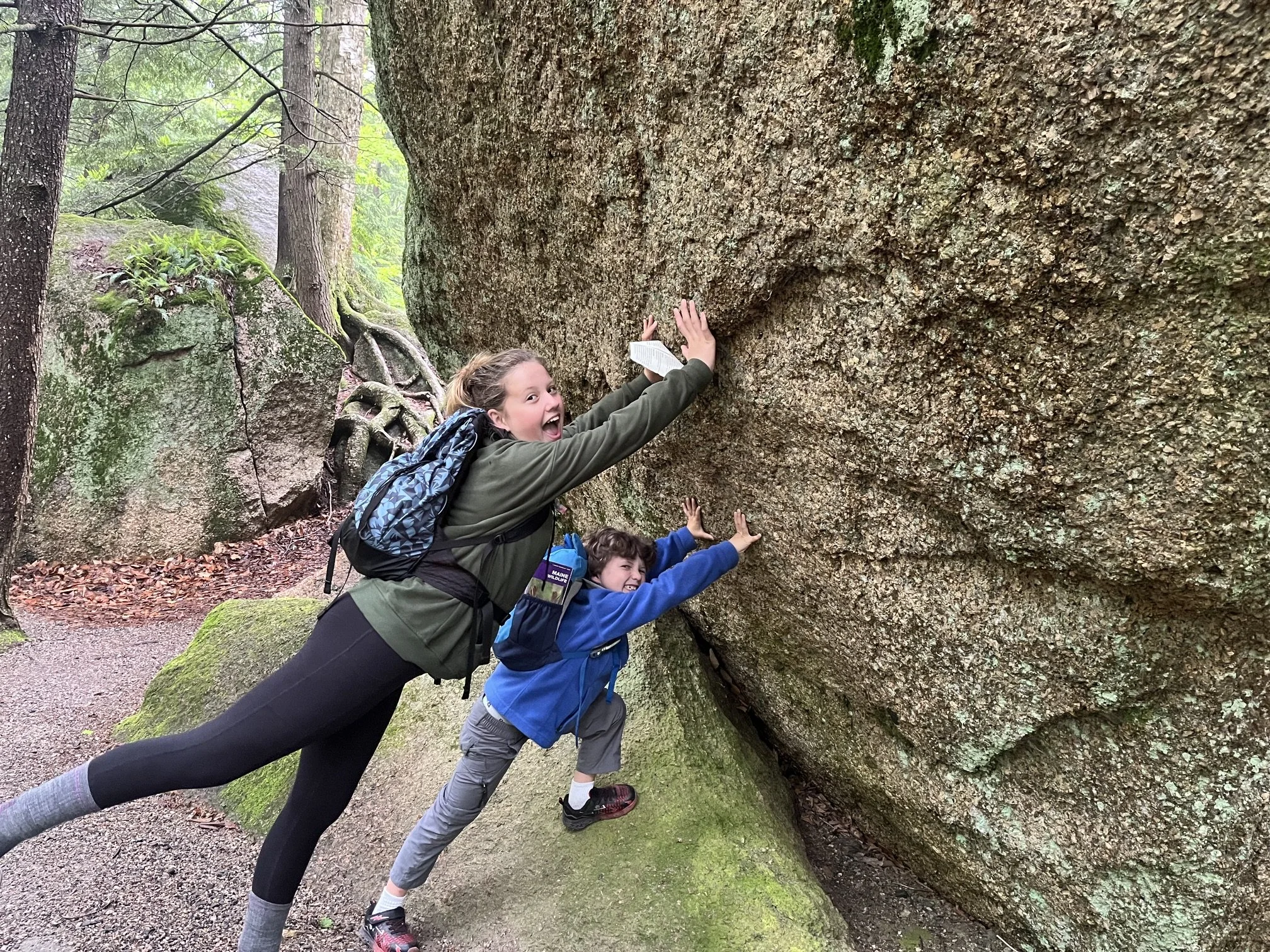 The author's children pretend to hold up a large glacial boulder on the Flume Gorge Trail