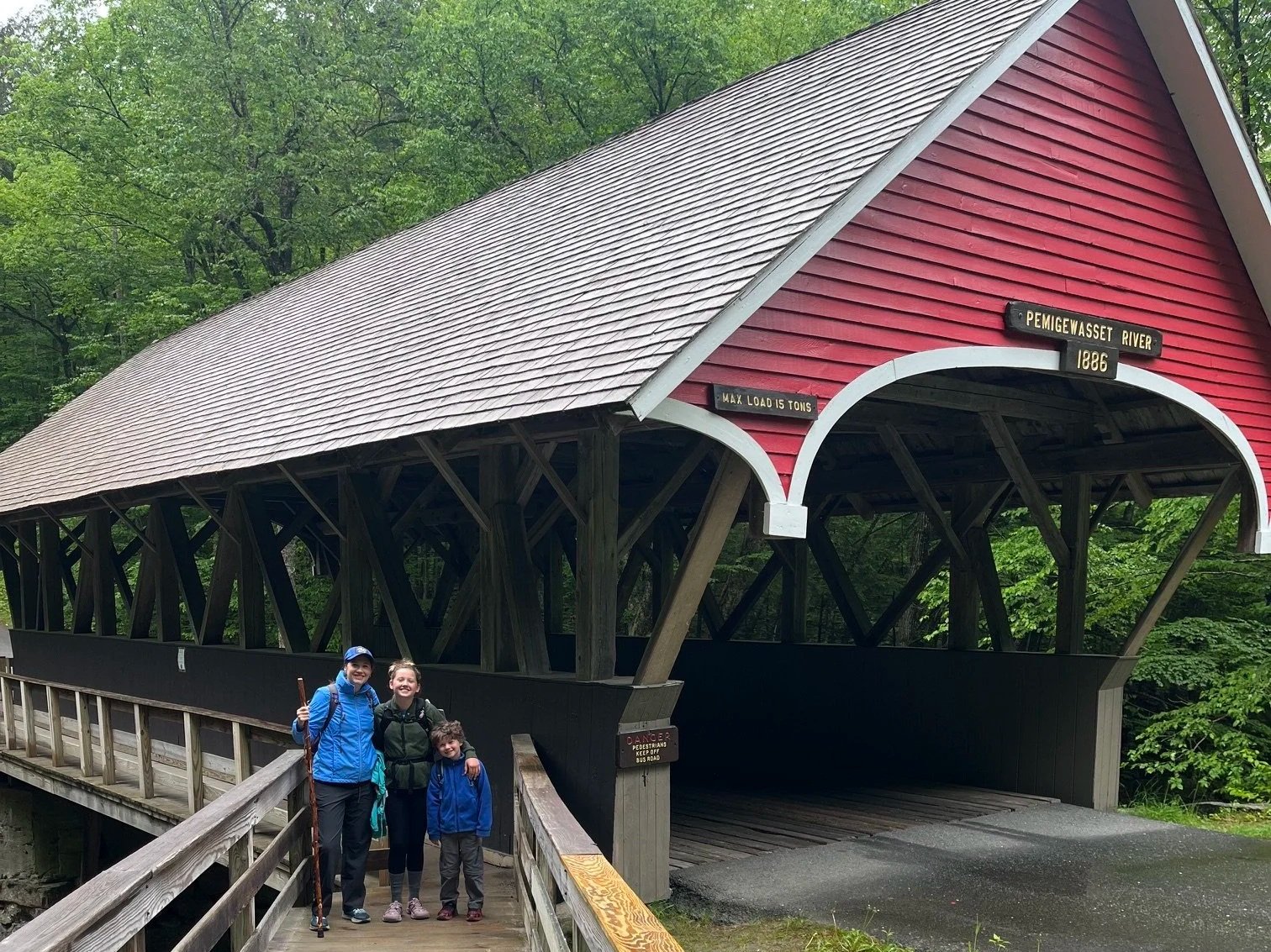The author and her 2 children standing on a wooden boardwalk next to a historic covered bridge on the Flume Gorge trail
