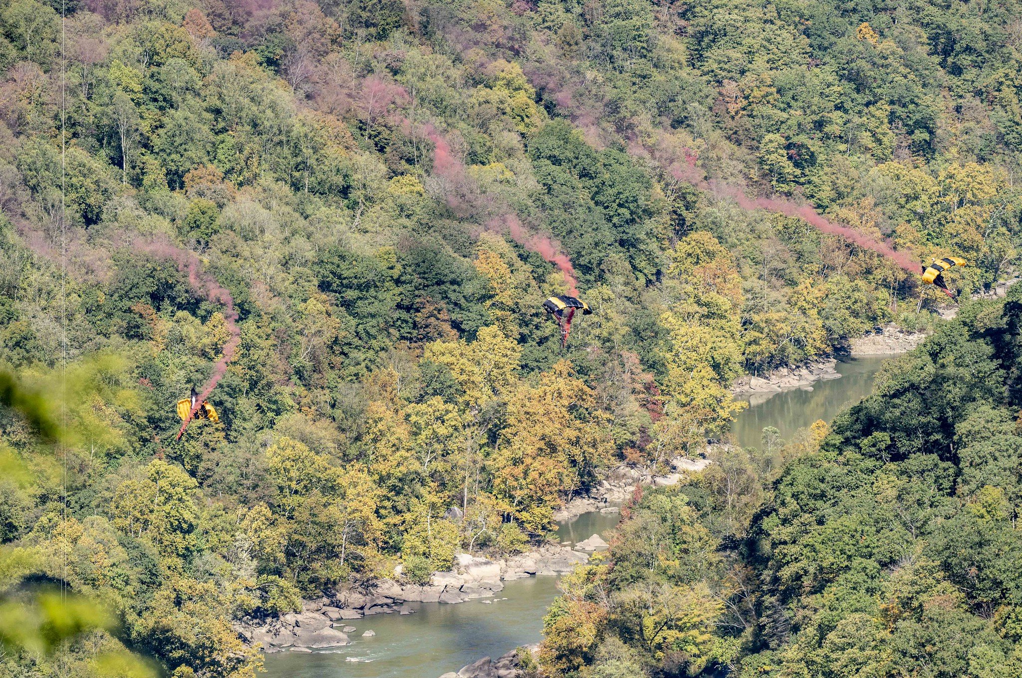 Base jumpers with red smoke flares as they descent into the gorge