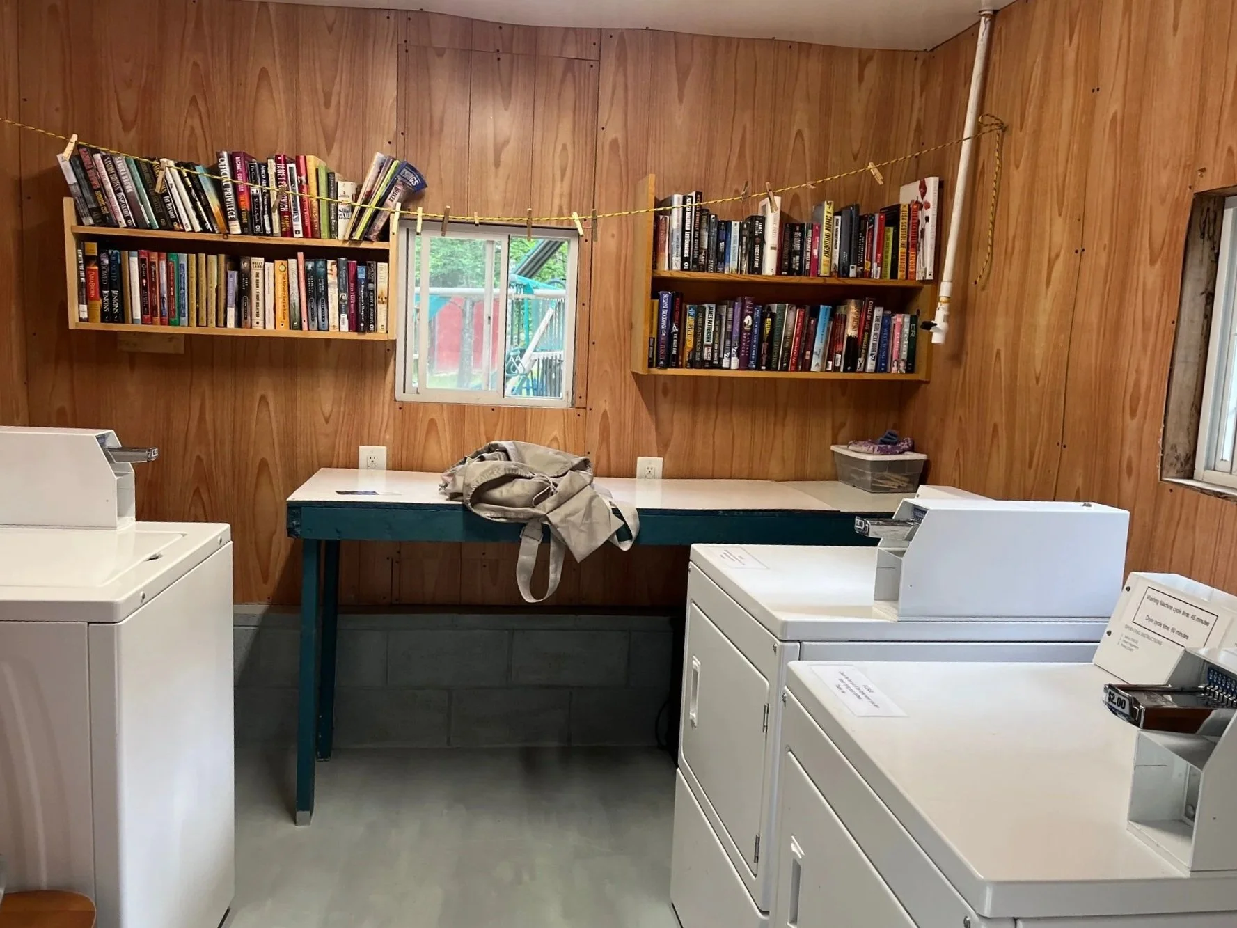 Laundry room with white washers and dryers. In the background is a folding table with a small window and bookshelves above