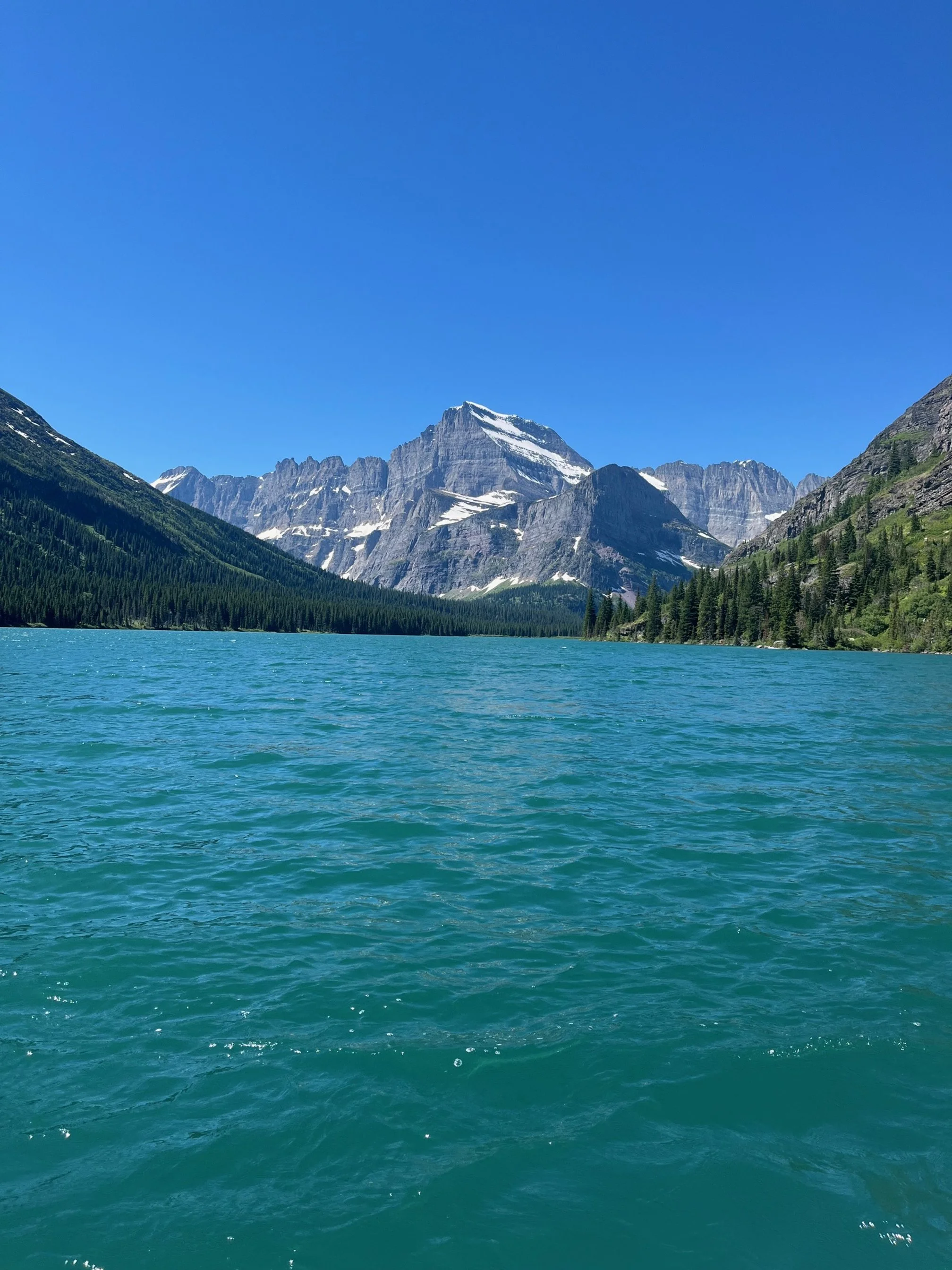 Turquoise lake in Glacier National Park with snow capped mountains and blue sky