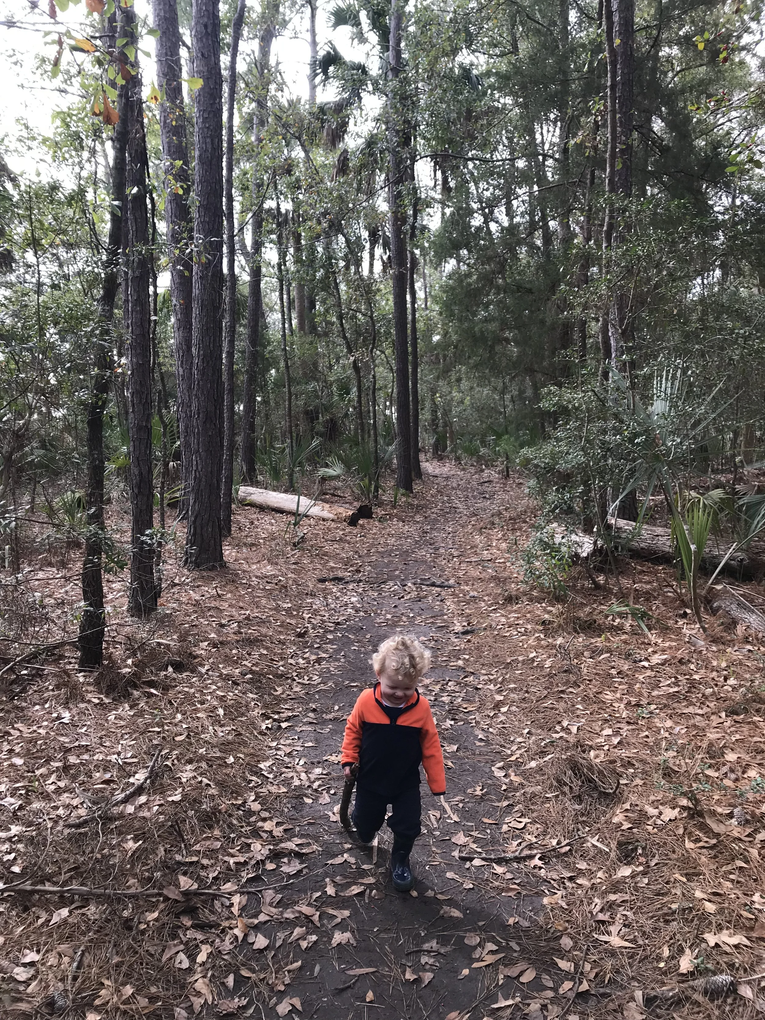 The author's son on a wide, flat trail holding a large stick in his right hand
