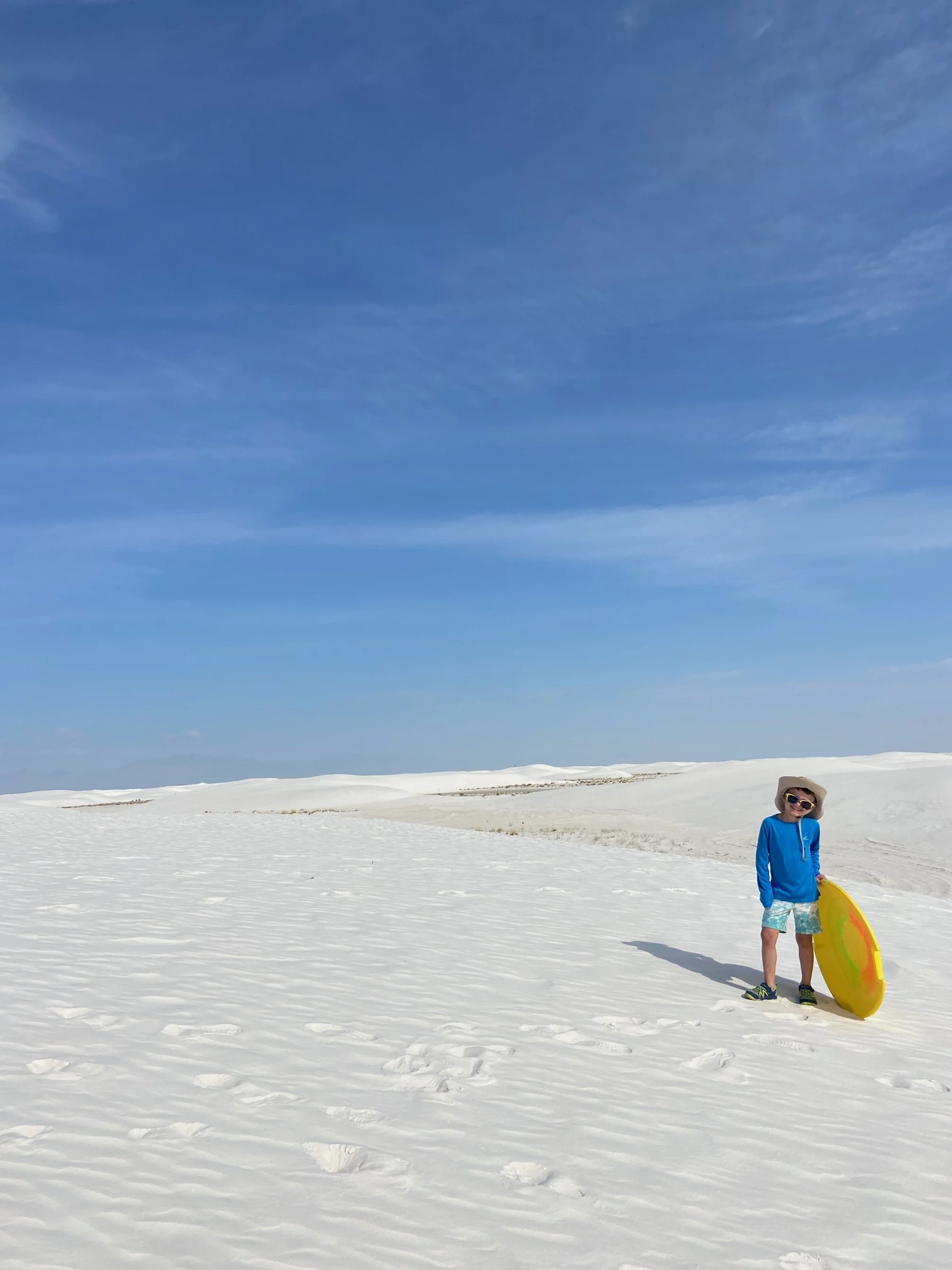 boy in blue sun shirt holds a yellow sand sled in White Sands National Park