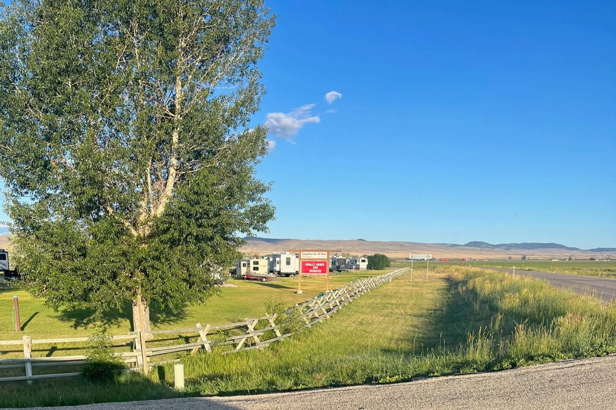 Large red campground sign by a split rail fence with rolling hills in the background