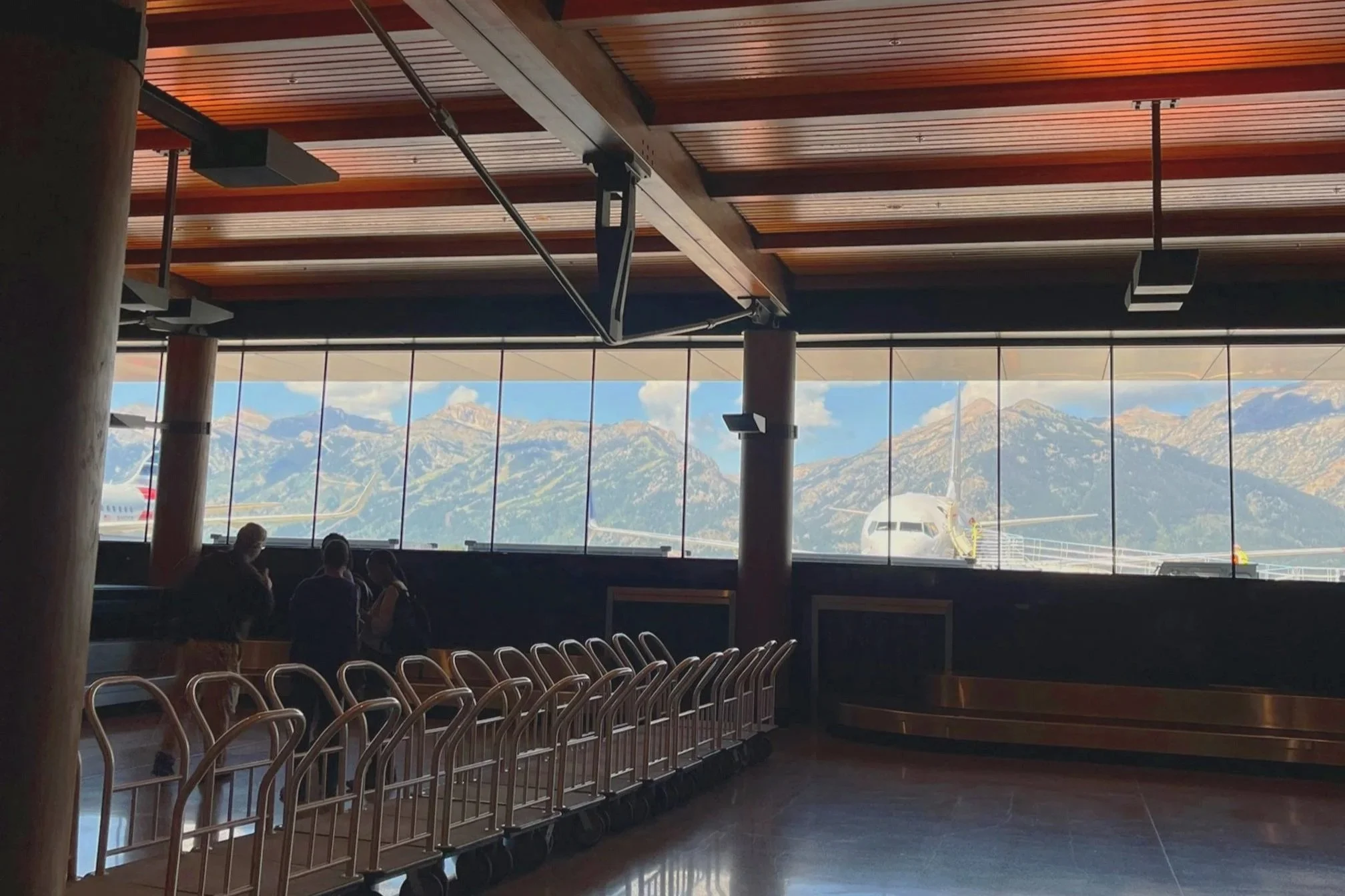An airplane is parked outside of the Jackson Hole airport with the mountain chain behind