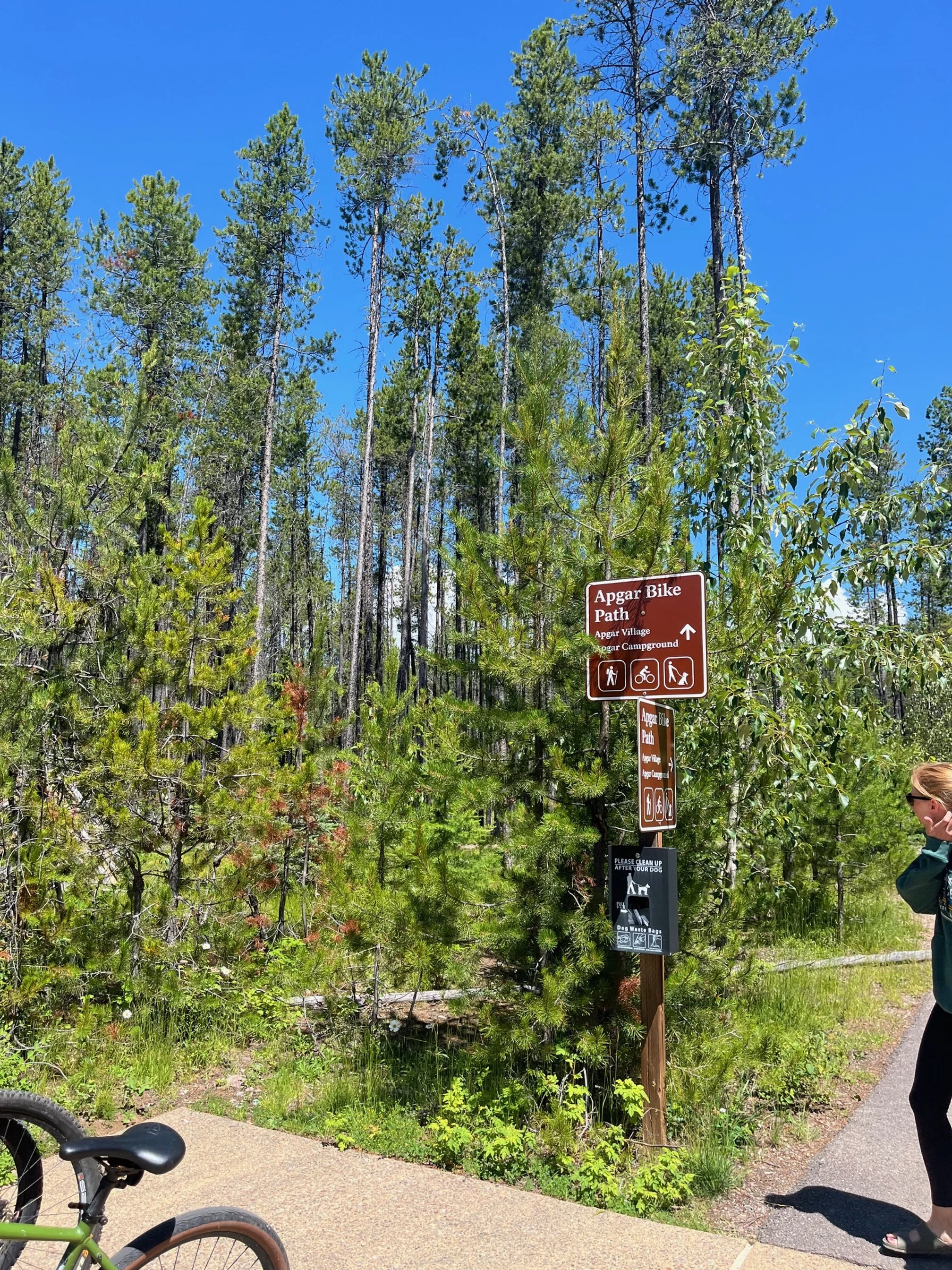 Brown metal sign pointing the way to the paved multi-use path near Apgar Village and the Visitors Center