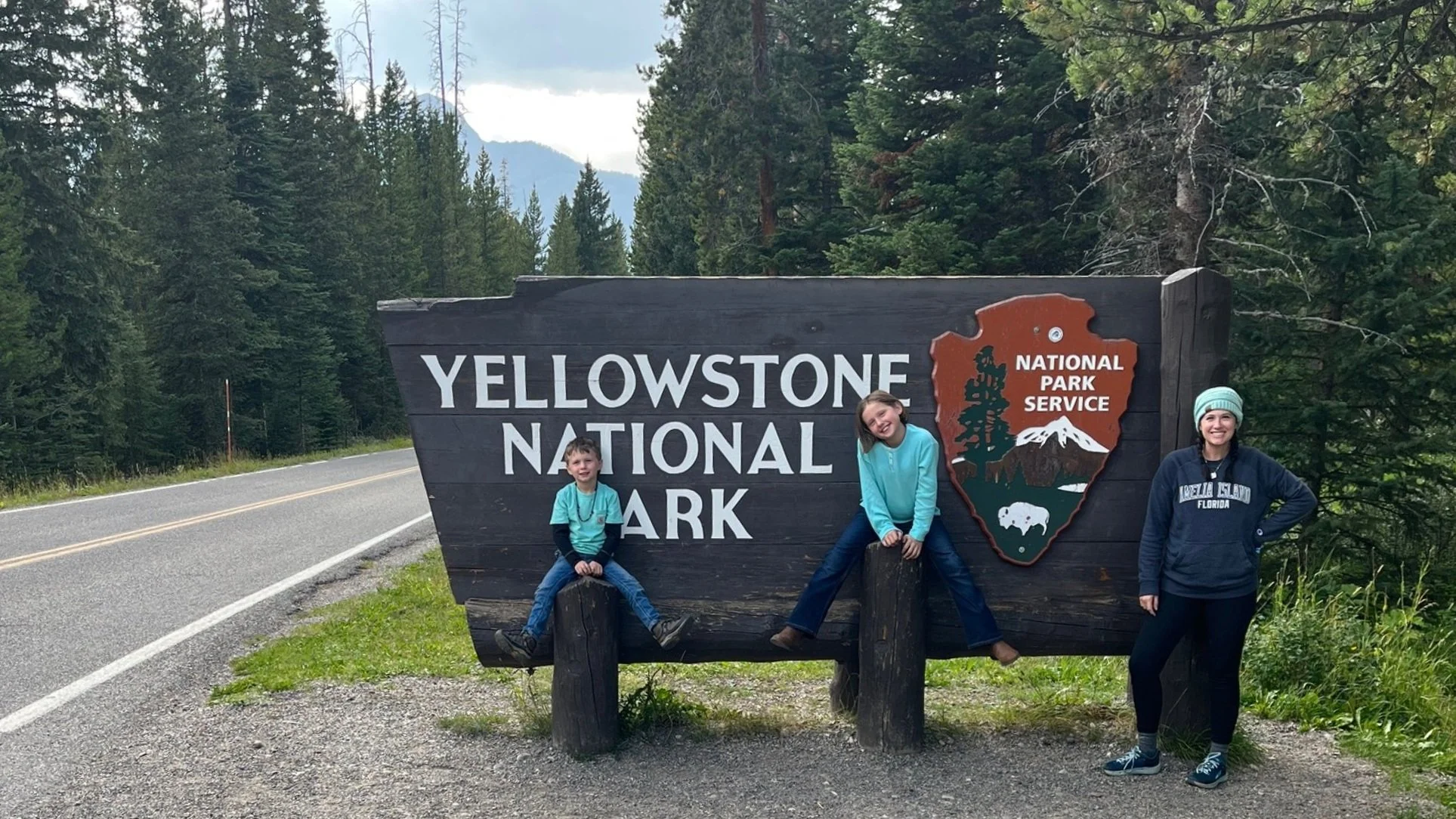 The author and her two kids stand next to the entrance sign for Yellowstone