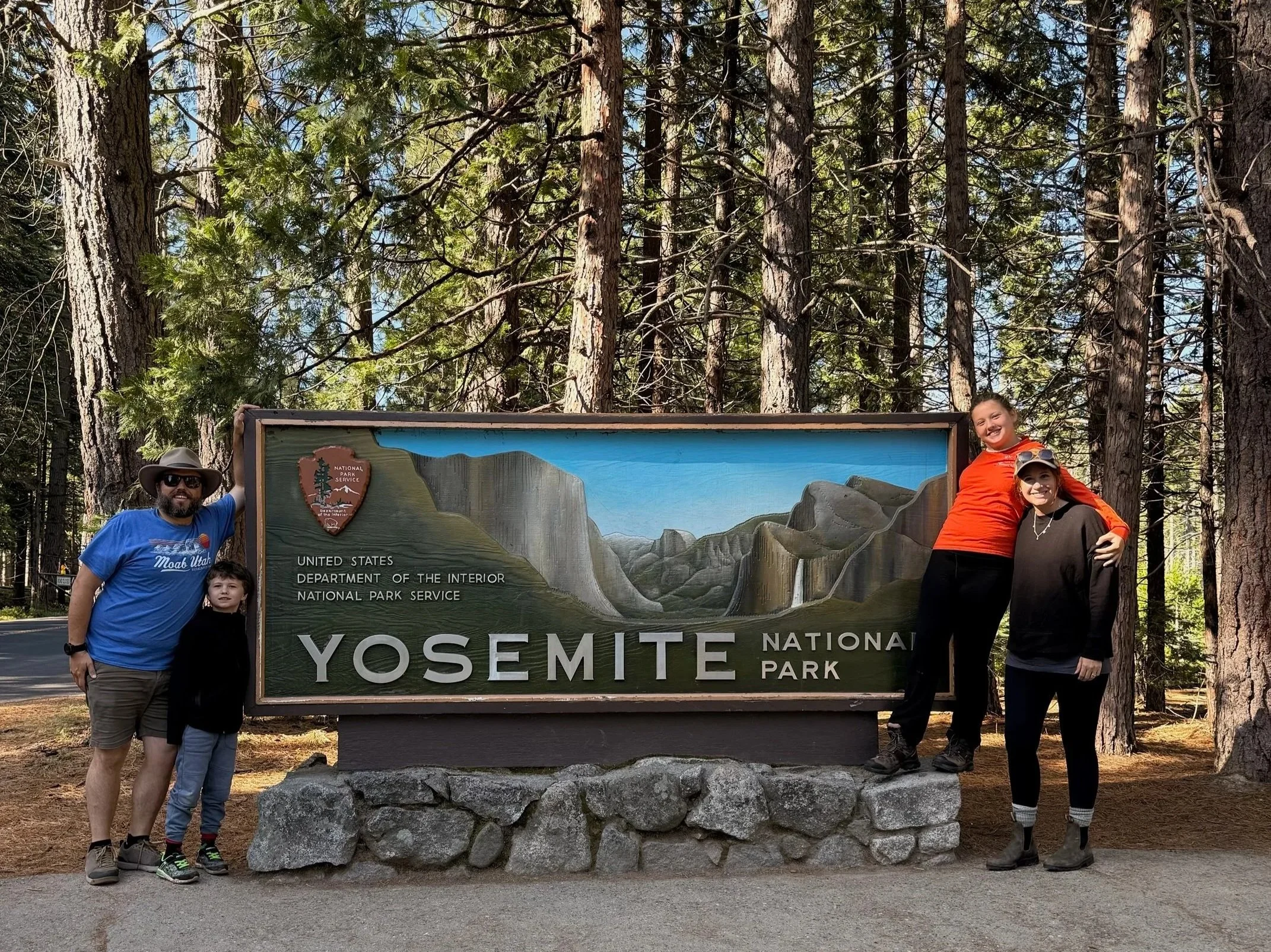 The author and her family standing next to a colorful wooden entrance sign for Yosemite National Park