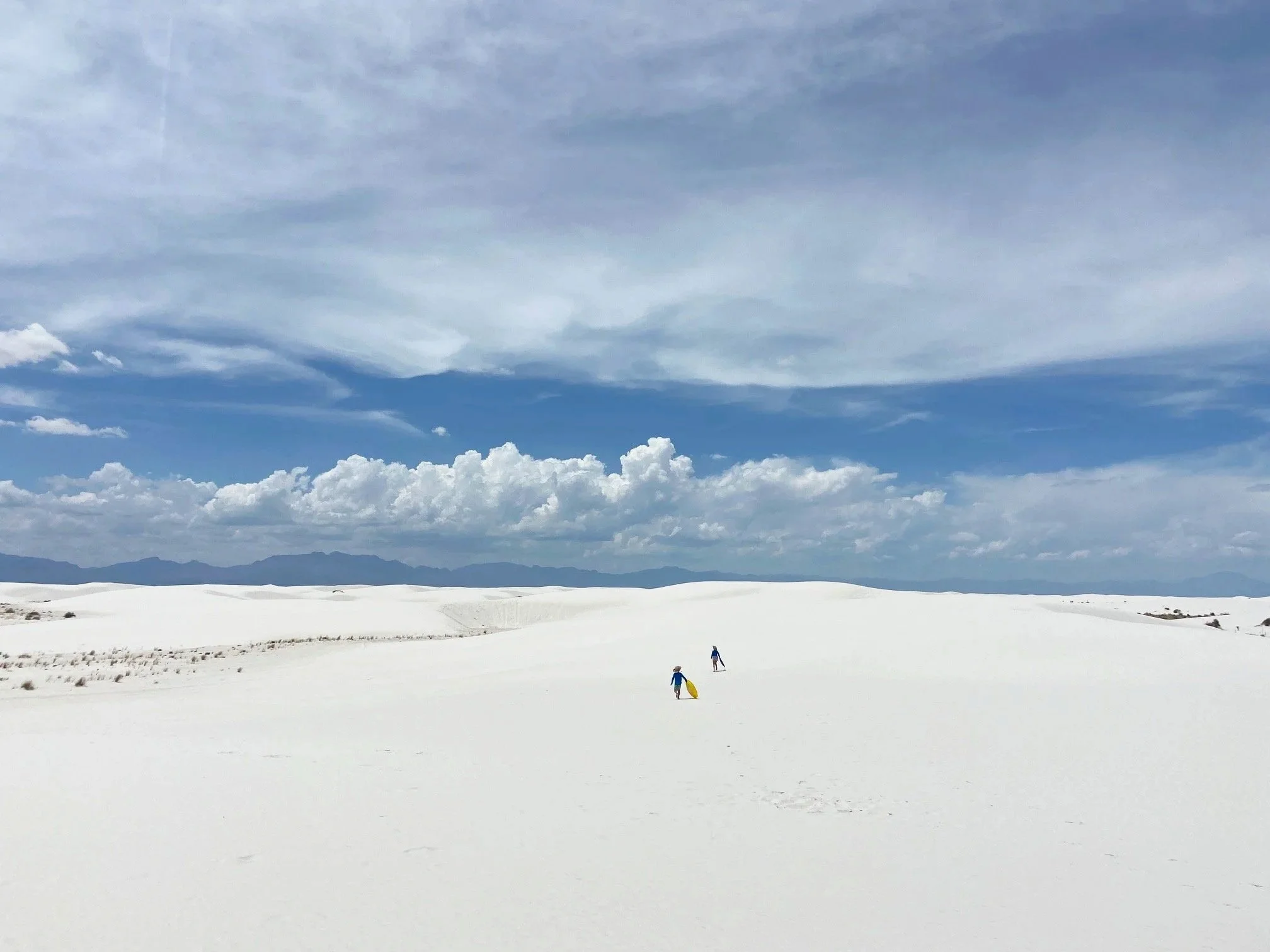 The author's children far out on a white dune field holding yellow sand saucers