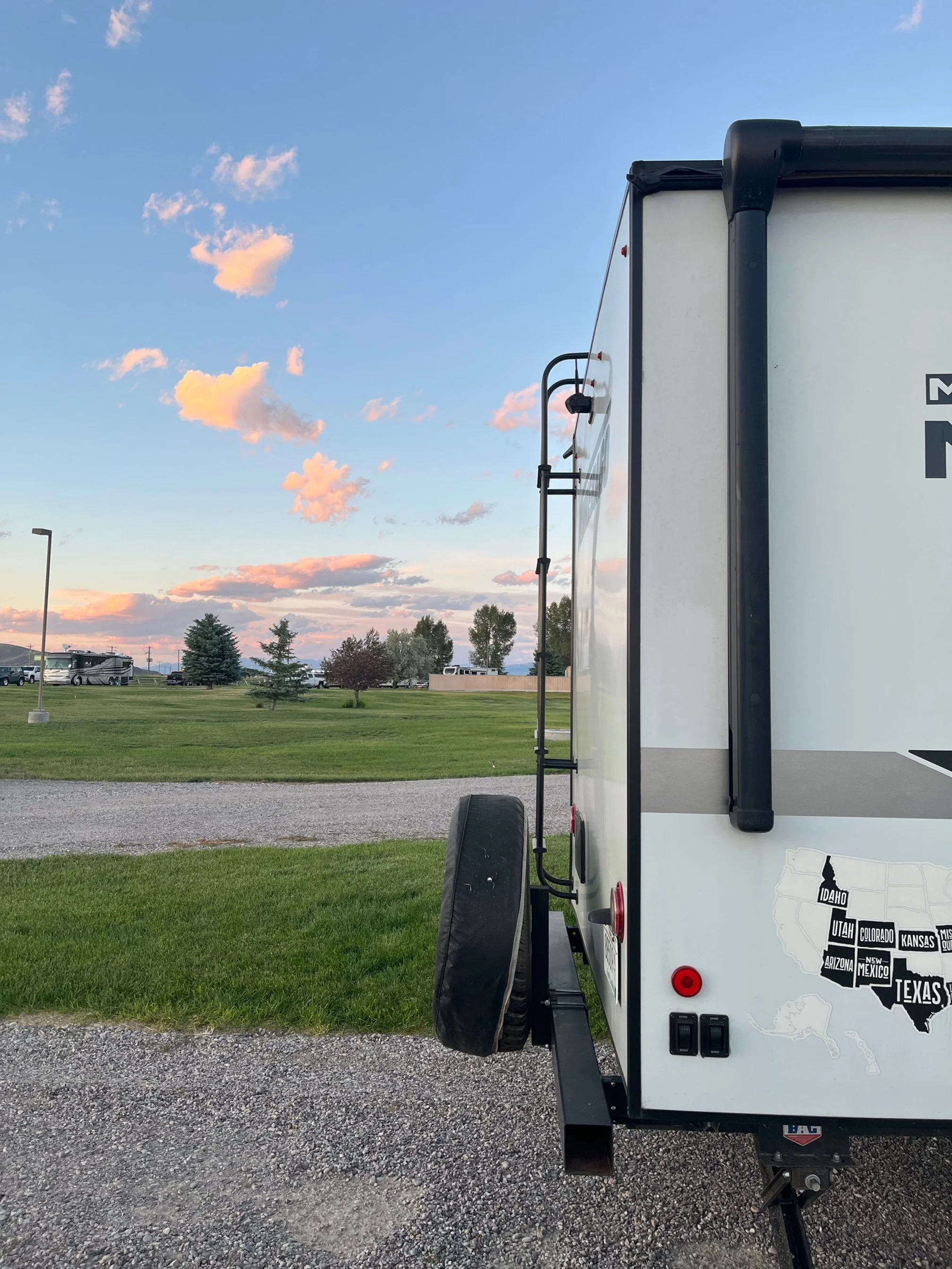 The bumper of the author's camper with gravel access road and grassy common area in background