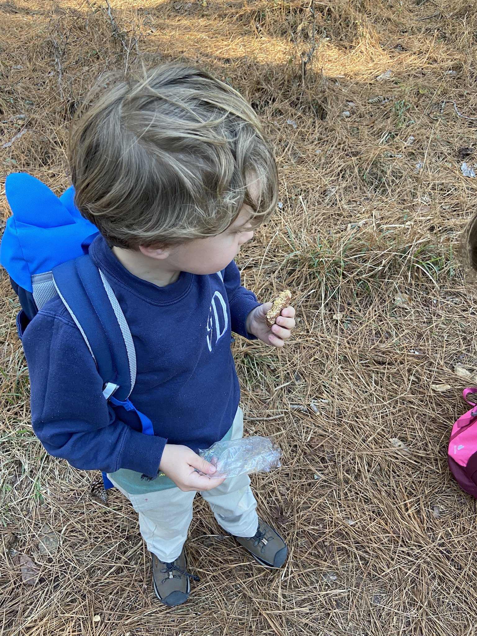 The author's son holding a cracker while wearing a blue day pack on the trail