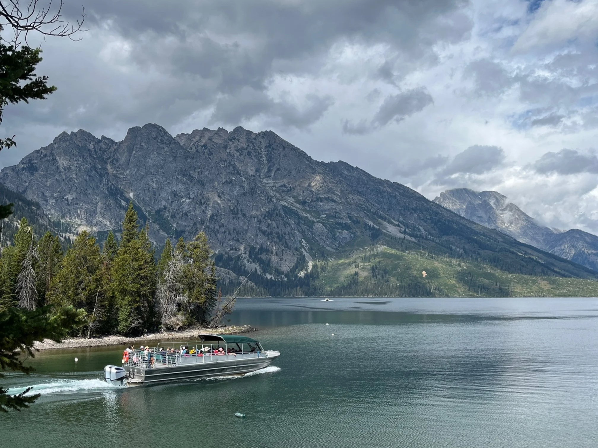 Boat tour cuts across Jenny Lake with the Grand Teton mountains in the distance