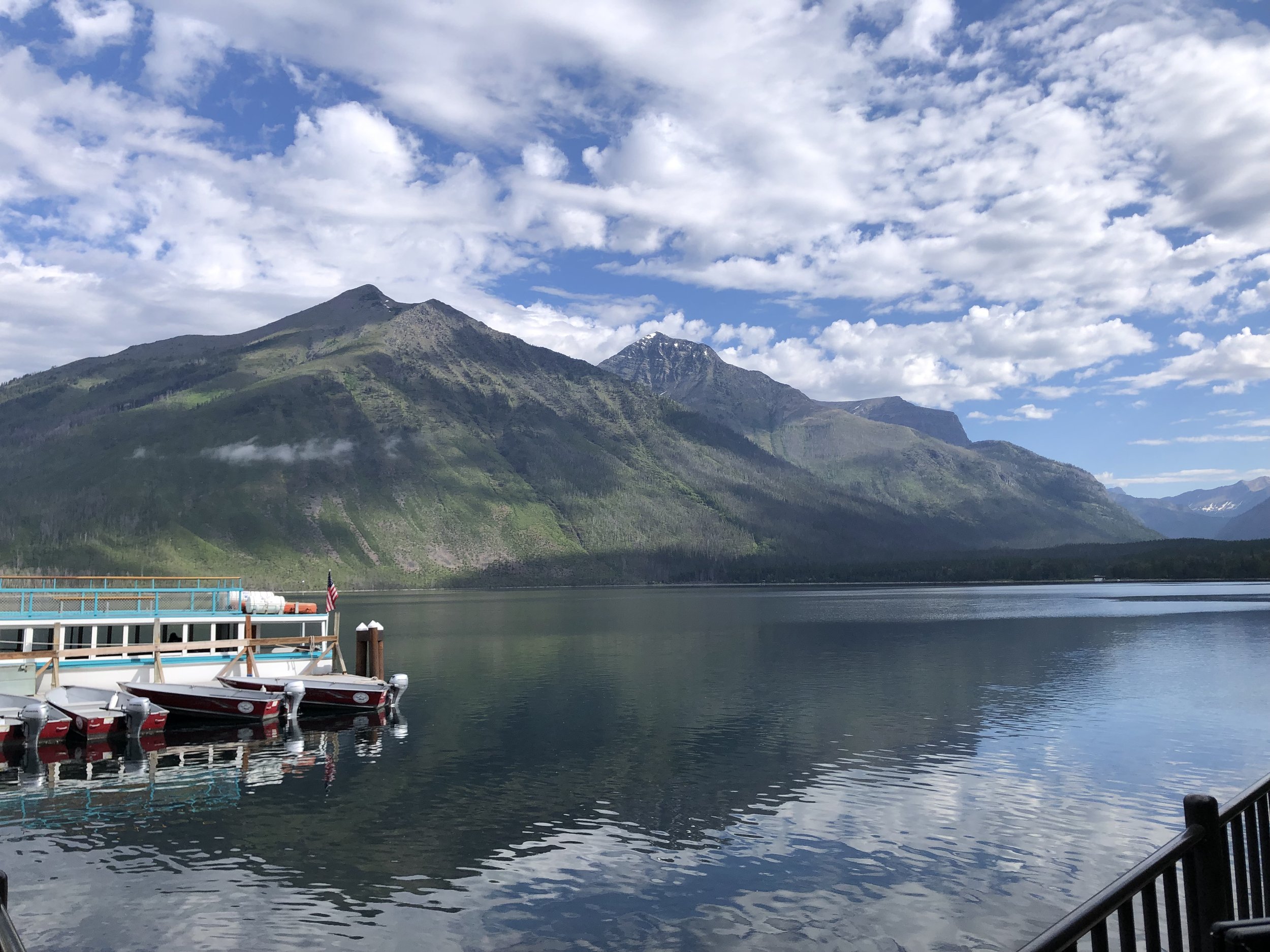 small turquoise and white boat docked in Lake McDonald with towering mountains on the far shore