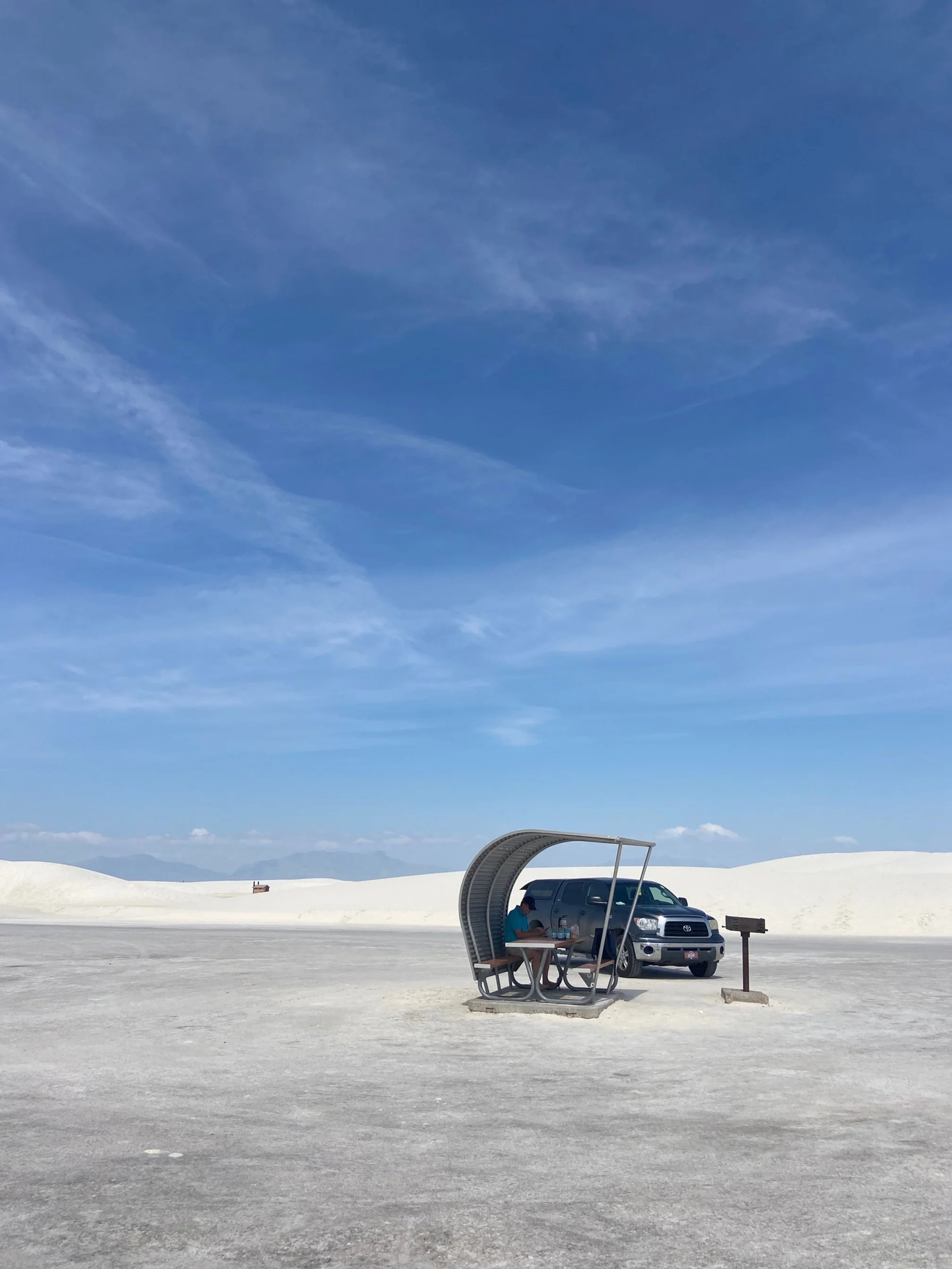 The author's blue truck parked behind a covered picnic area amid the dunes of White Sands National Park