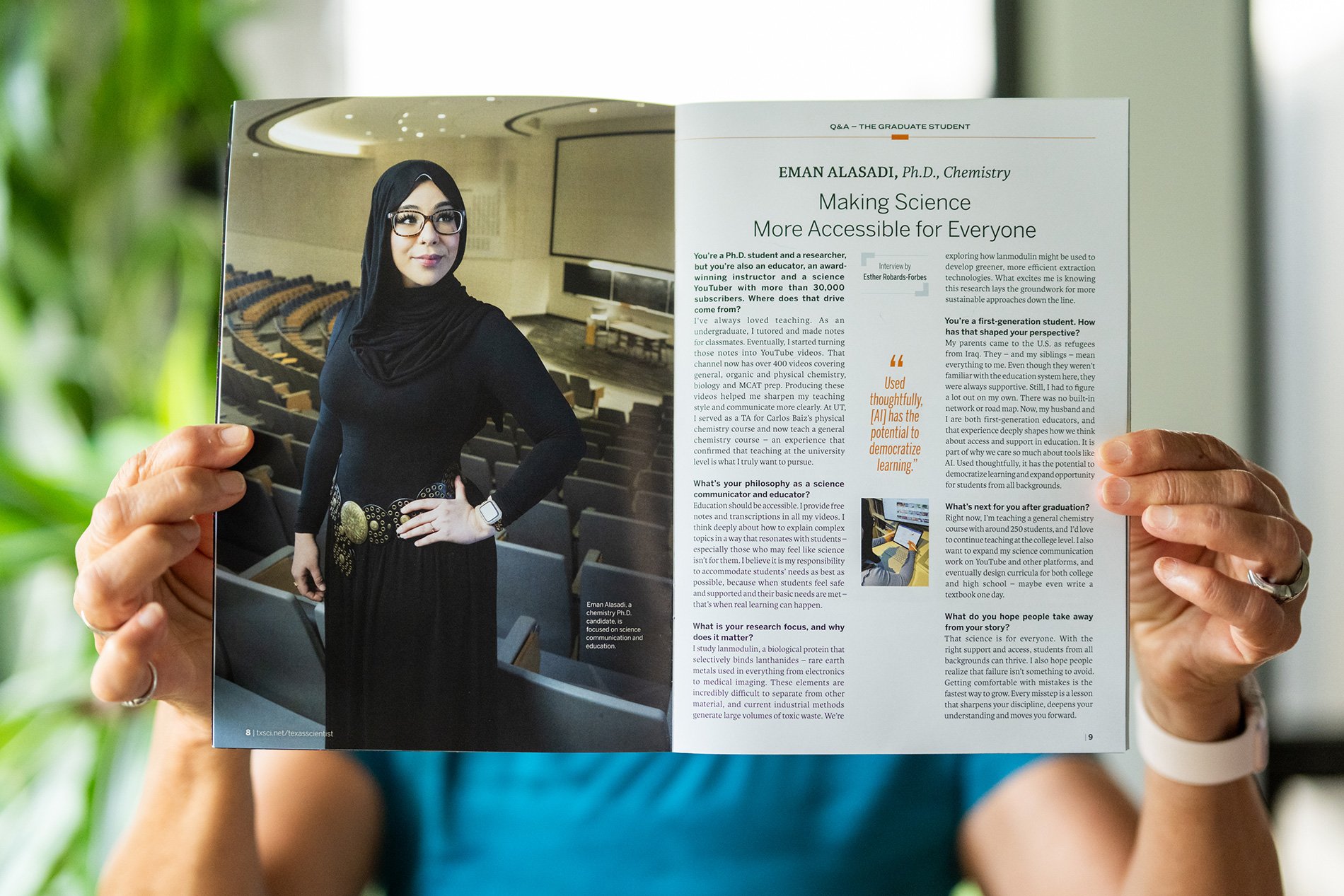 A person holding an open magazine showing an article with a photograph of a woman wearing hijab and glasses in an auditorium and the article discusses making science accessible. The woman in the photo is identified as Eman Alasadi, a Ph.D. candidate in chemistry.