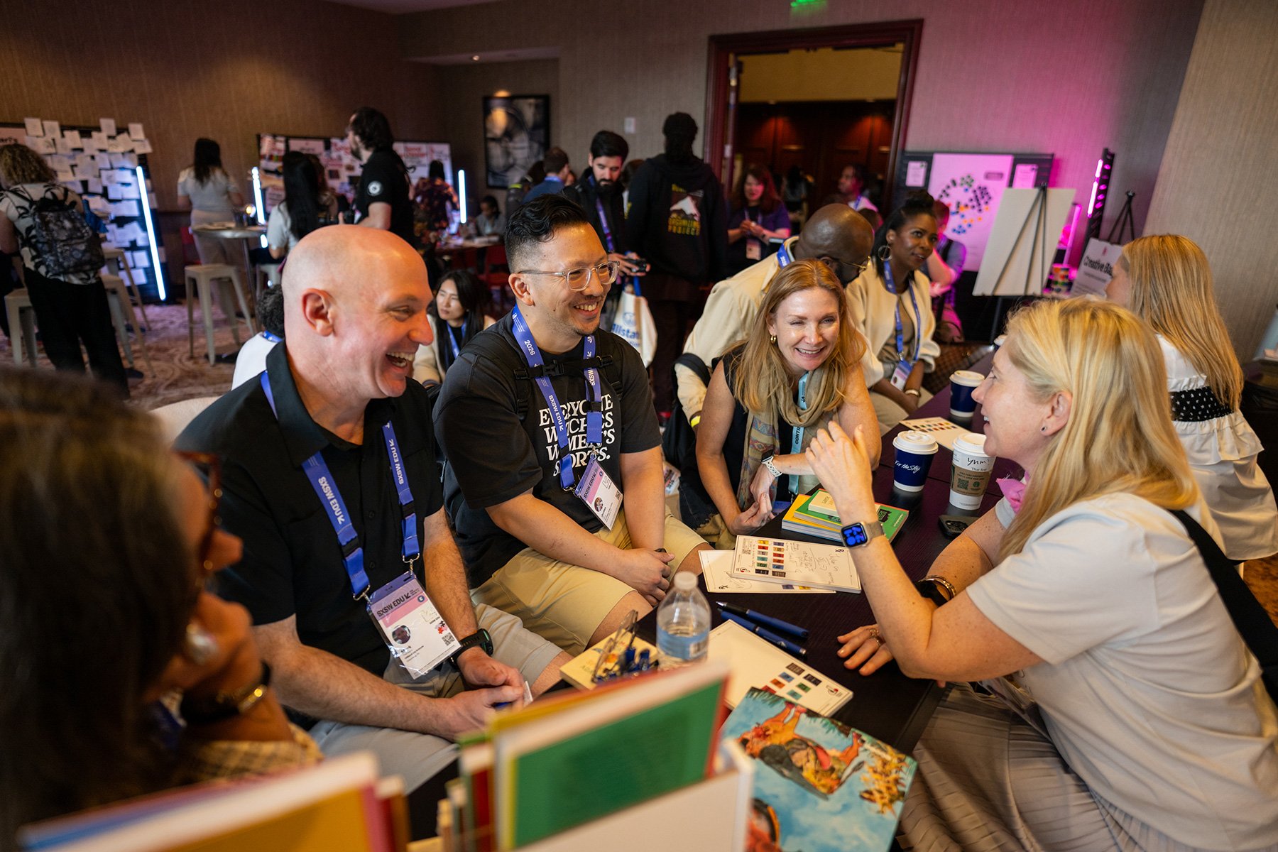 A candid close-up of diverse attendees in a lively table workshop discussion. Authentic networking, laughter, and collaborative interaction, with visible conference badges.