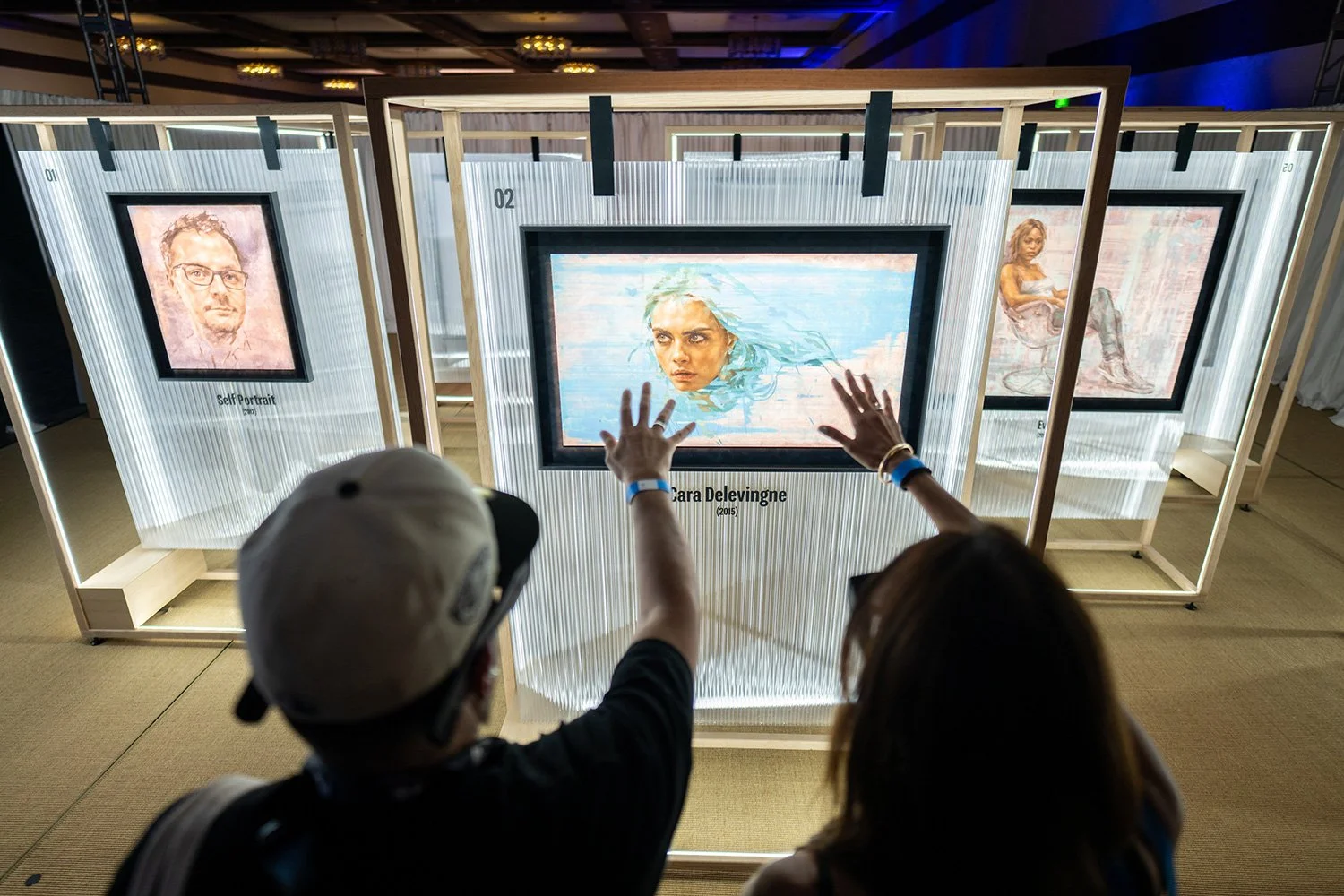Two attendees at SXSW interacting with a modern digital art exhibit featuring glowing, framed portraits in a darkened event space