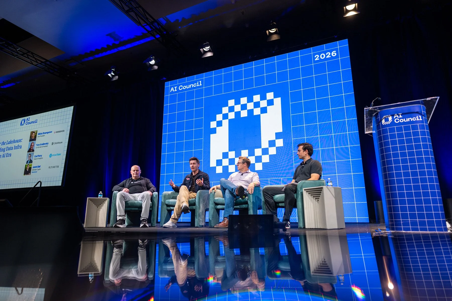 Austin corporate event photography capturing an expert panel discussion with four speakers seated on a polished stage in front of a massive, custom-branded blue digital backdrop at the AI Council 2026 conference.