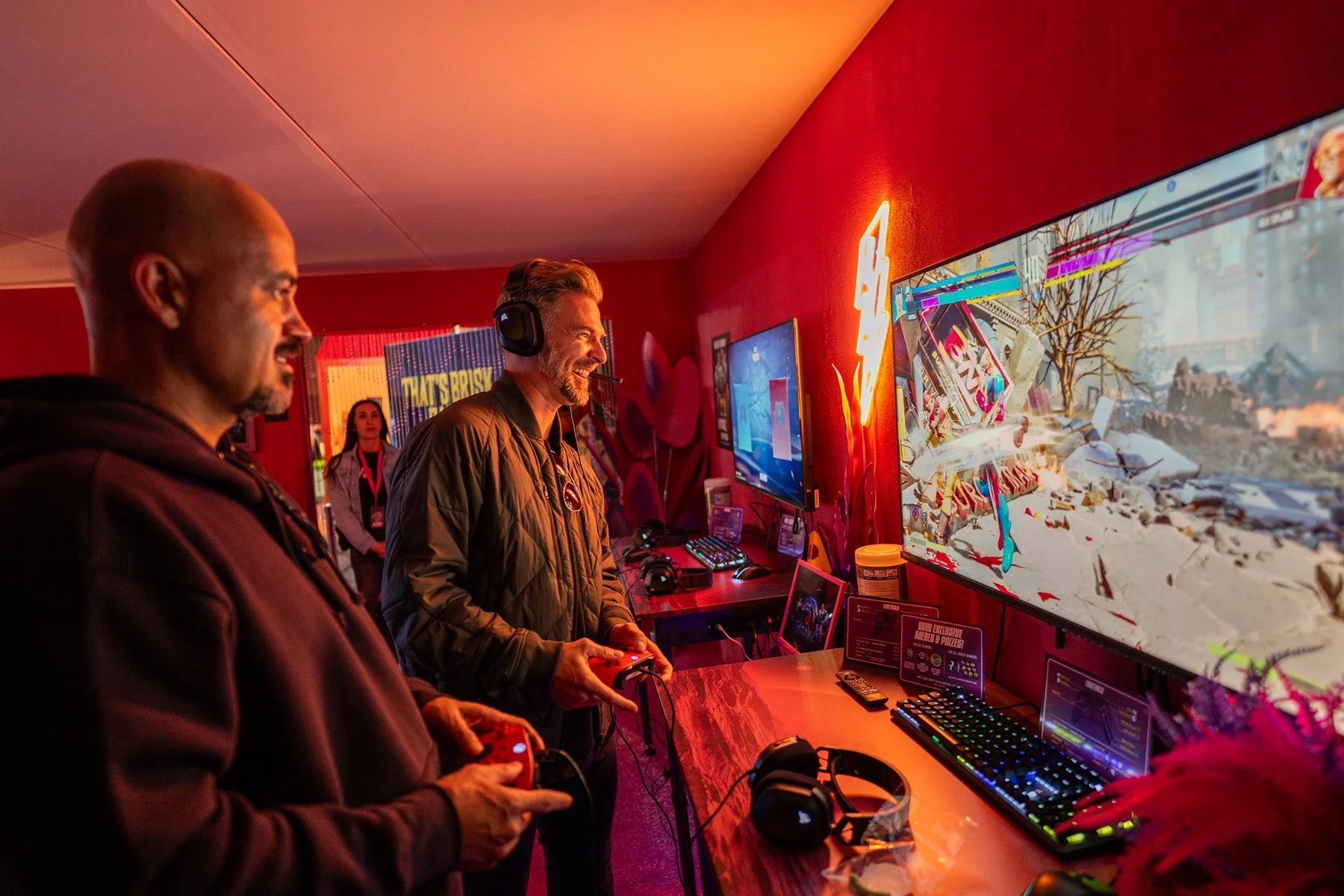 SXSW 2026 video game lounge in Austin, Texas. Two men at a console with red neon light and pro gear. Authentic attendee joy at a brand event. High-end event photography by Tico Mendoza Studios.