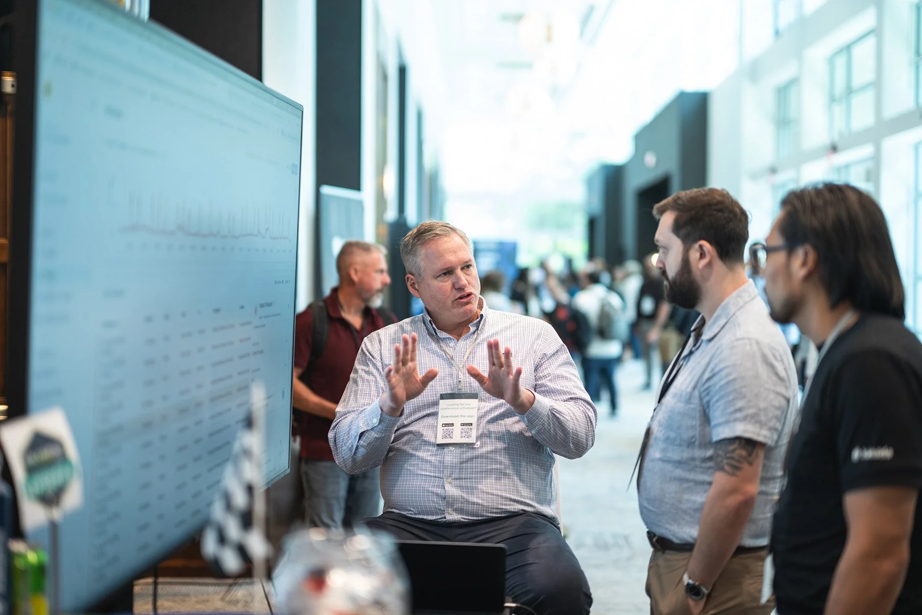 Corporate event photography in Austin capturing a professional presentation and discussion in front of a digital display screen at a conference booth.