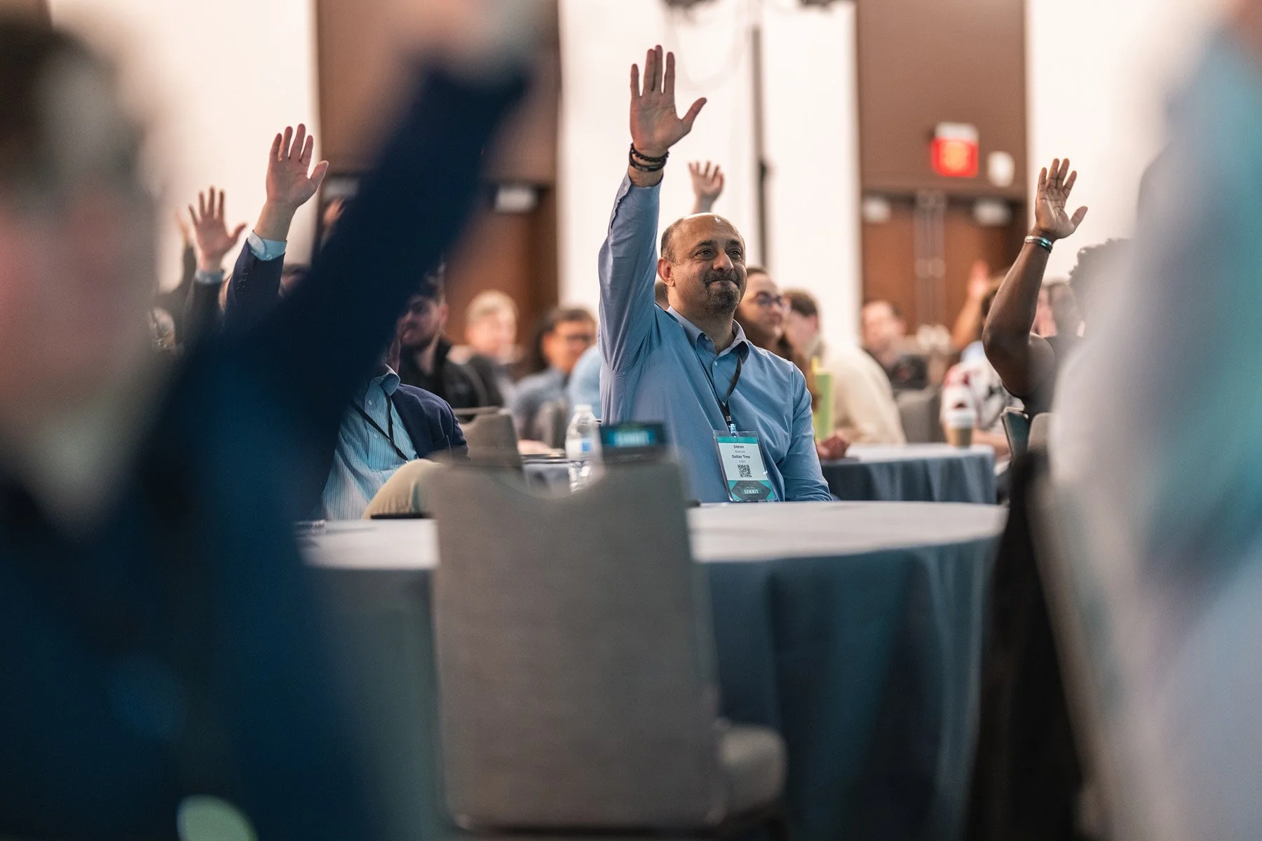 Engaged audience at an Austin corporate event presentation with their hands raised in response to a speaker's question in a conference hall.