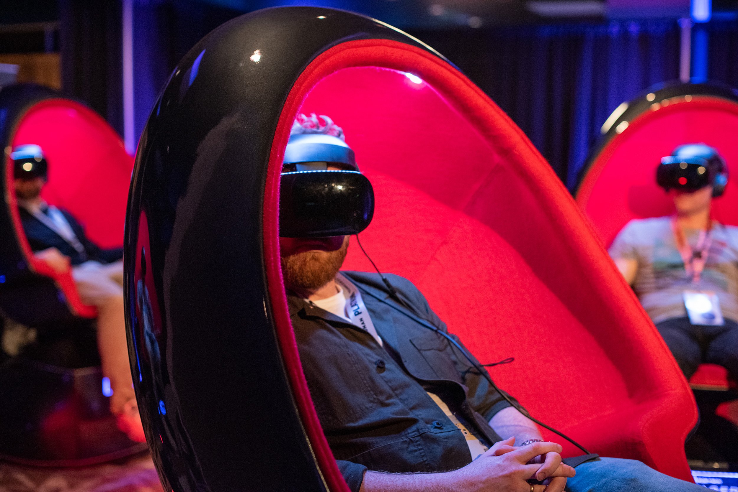 People sitting inside individual red pods, engaging with virtual reality headsets at a tech event or exhibition.