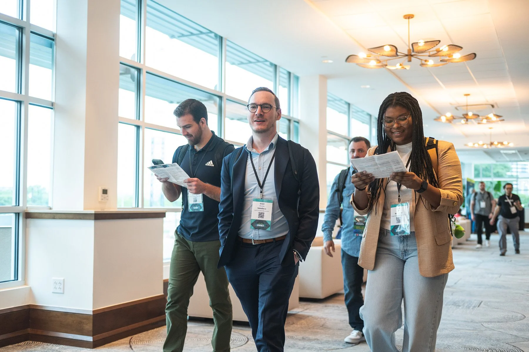 Austin corporate event photography of attendees walking and reviewing materials in a modern, bright conference center hallway with floor-to-ceiling windows.