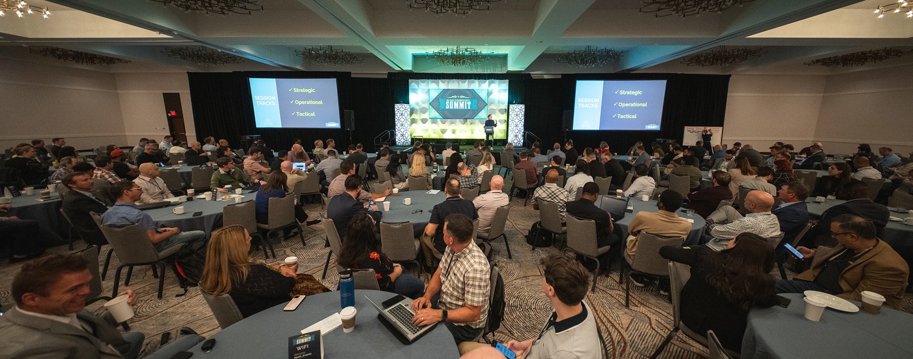 Wide angle photography of a large corporate event ballroom in Austin, Texas, showing attendees at round tables watching a main stage presentation.