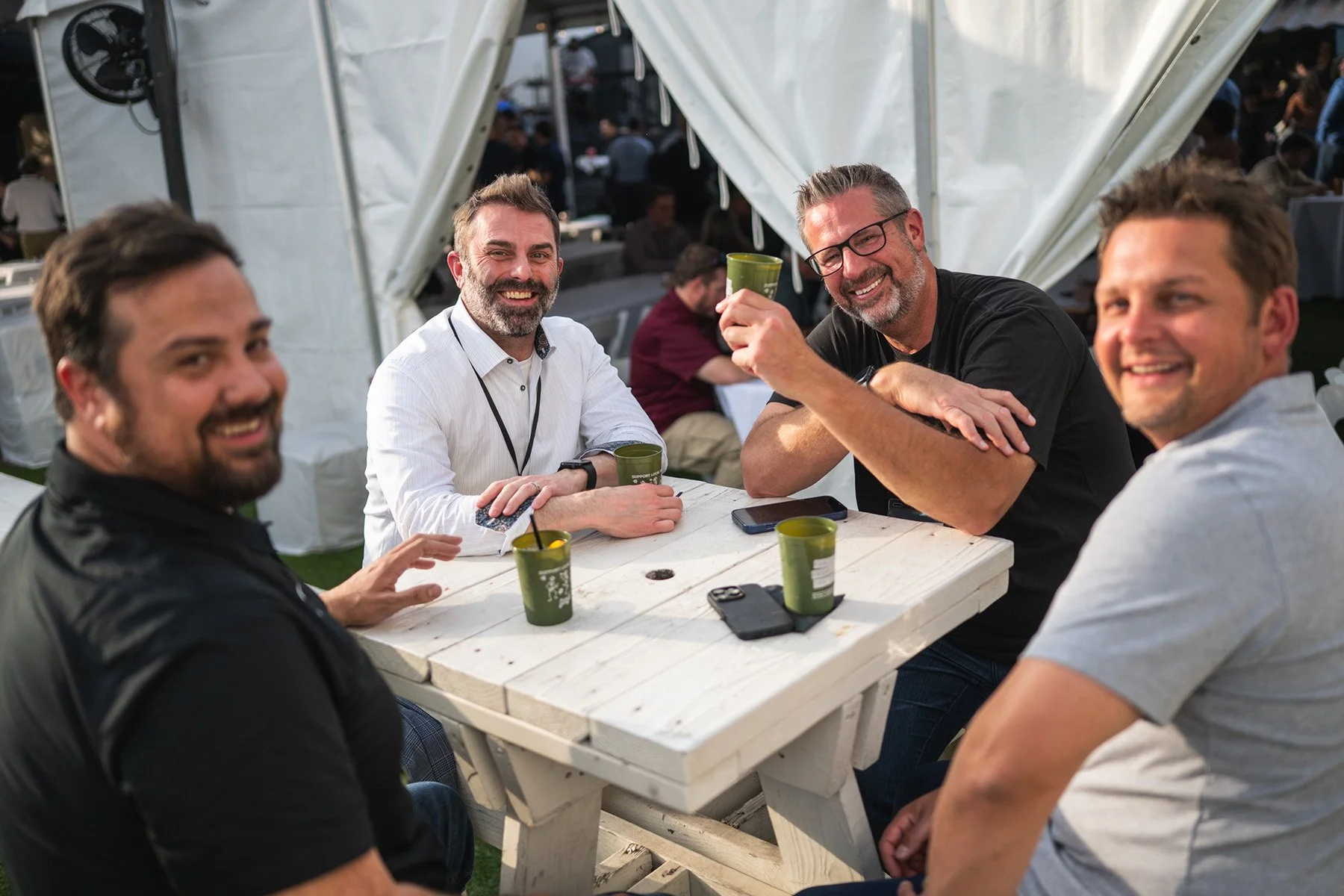 Candid networking photography at an Austin corporate event featuring four professionals smiling and enjoying drinks around a table at an outdoor reception.