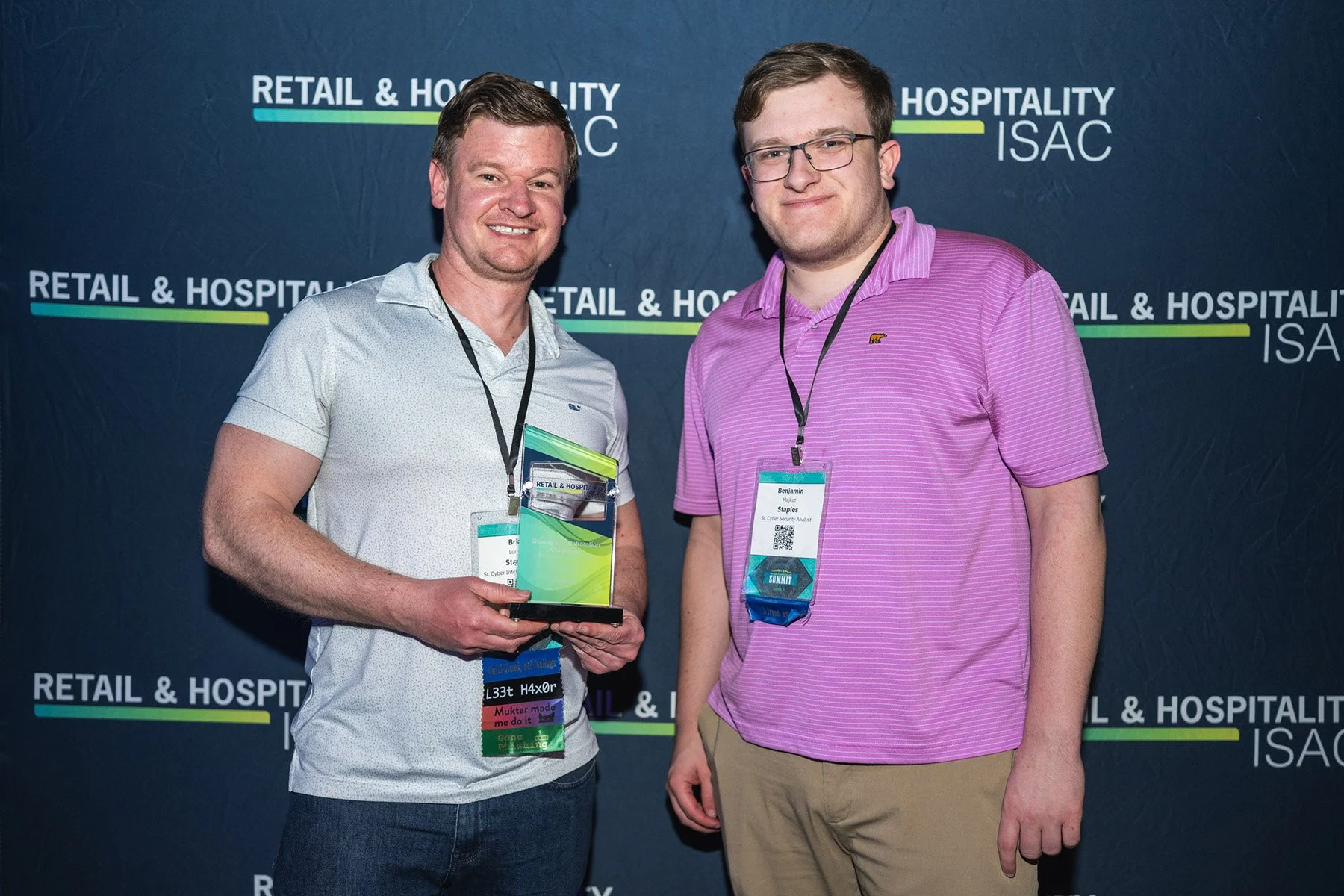 Step-and-repeat corporate event photography in Austin showing two attendees smiling and posing with an award in front of a branded Retail & Hospitality ISAC conference backdrop.