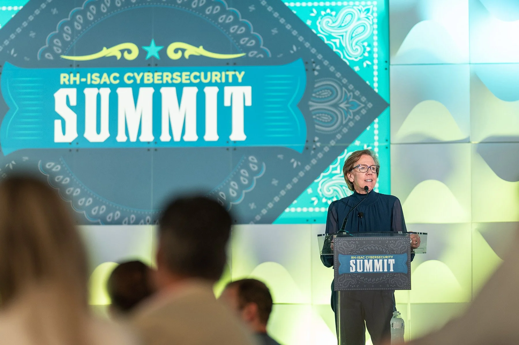 Female keynote speaker delivering a presentation at a podium during an Austin corporate summit with custom stage branding.