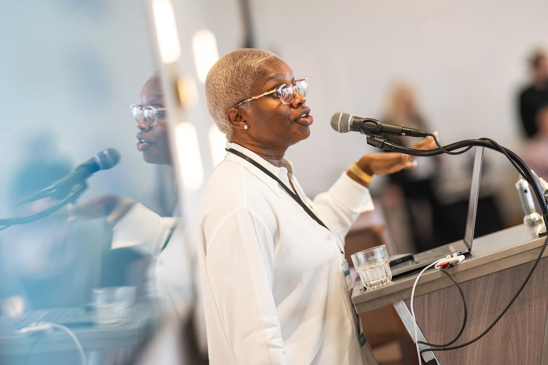 Creative corporate event photography in Austin showing a female presenter speaking passionately into a microphone at a podium during a conference session.