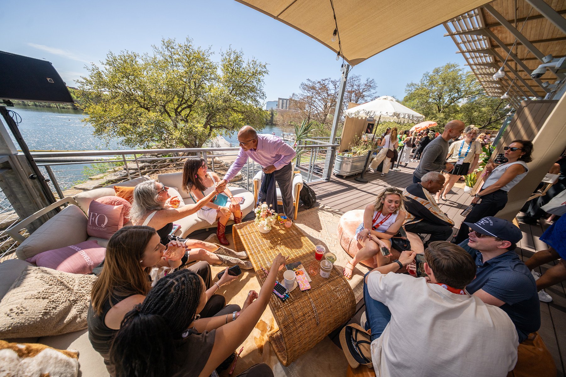SXSW 2026 event at The Female Quotient lounge in Austin, Texas. A professional handshake between attendees on a sunlit waterfront deck. High-end corporate event photography for brand activations by Tico Mendoza Studios.