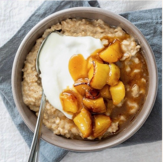 A bowl of oatmeal topped with a dollop of yogurt, caramelized peaches, and syrup.
