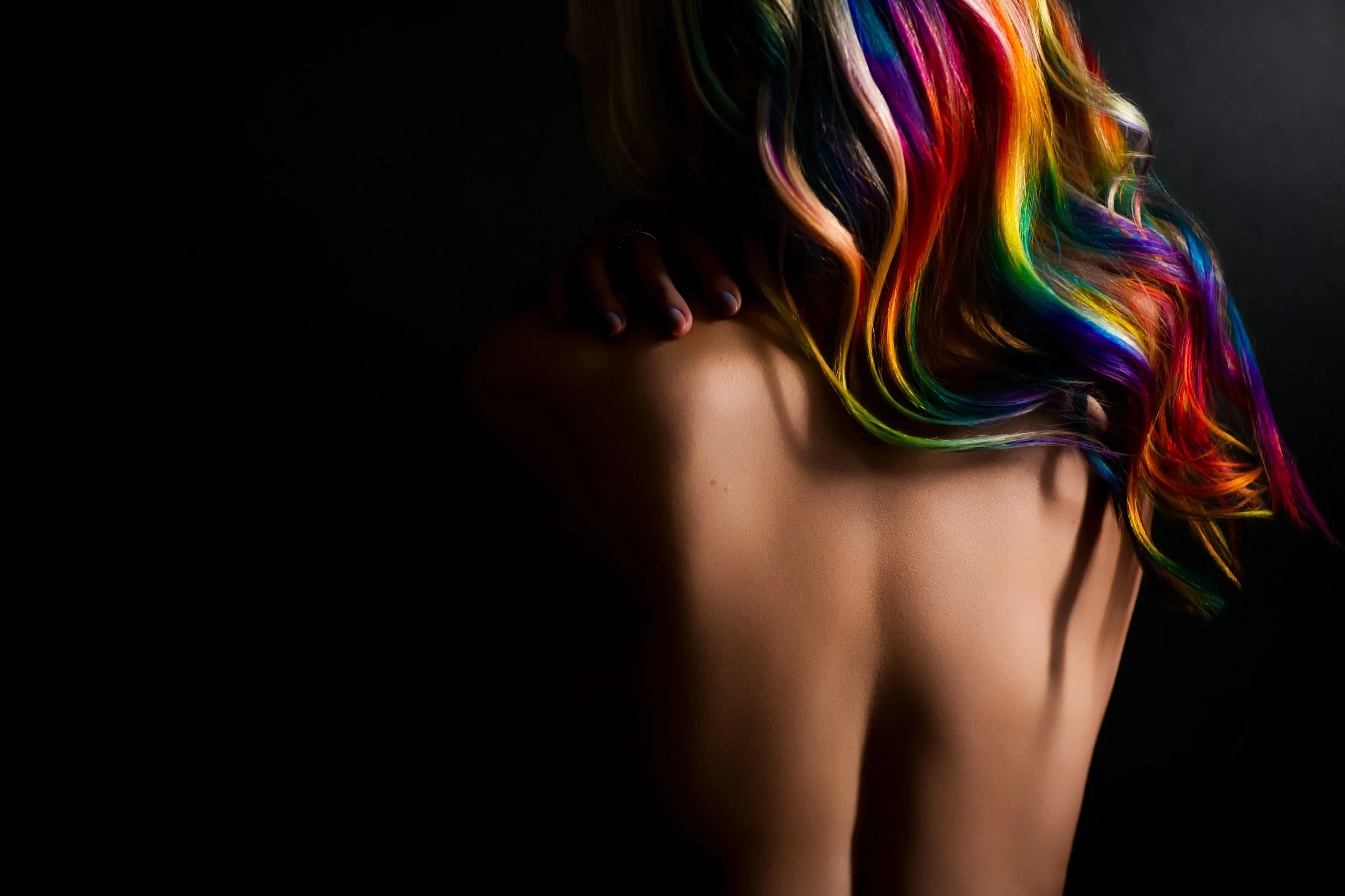A person with long, rainbow-colored hair covering their face, with a dark background.