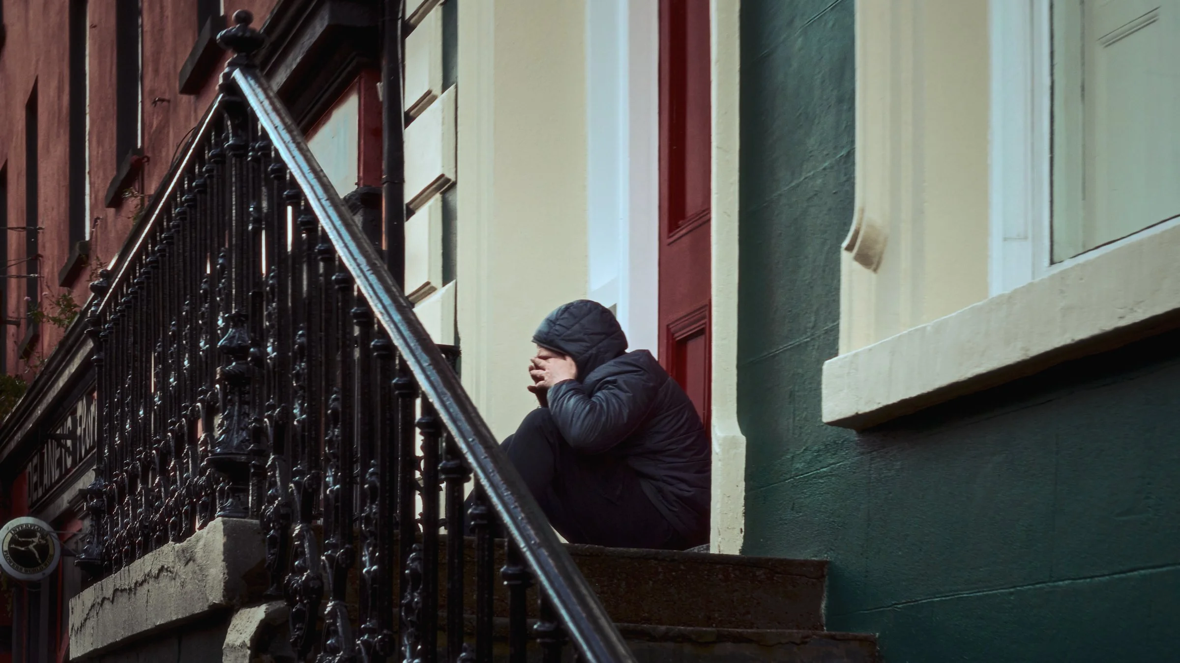 One Take - Ireland "The Call", Waterford City, Co. Waterford, Ireland 2024. A cinematic color photograph of a person sits on steps rubbing his eyes while talking on a mobile phone. It looks like he may be crying. Photograph by Dave Haworth.