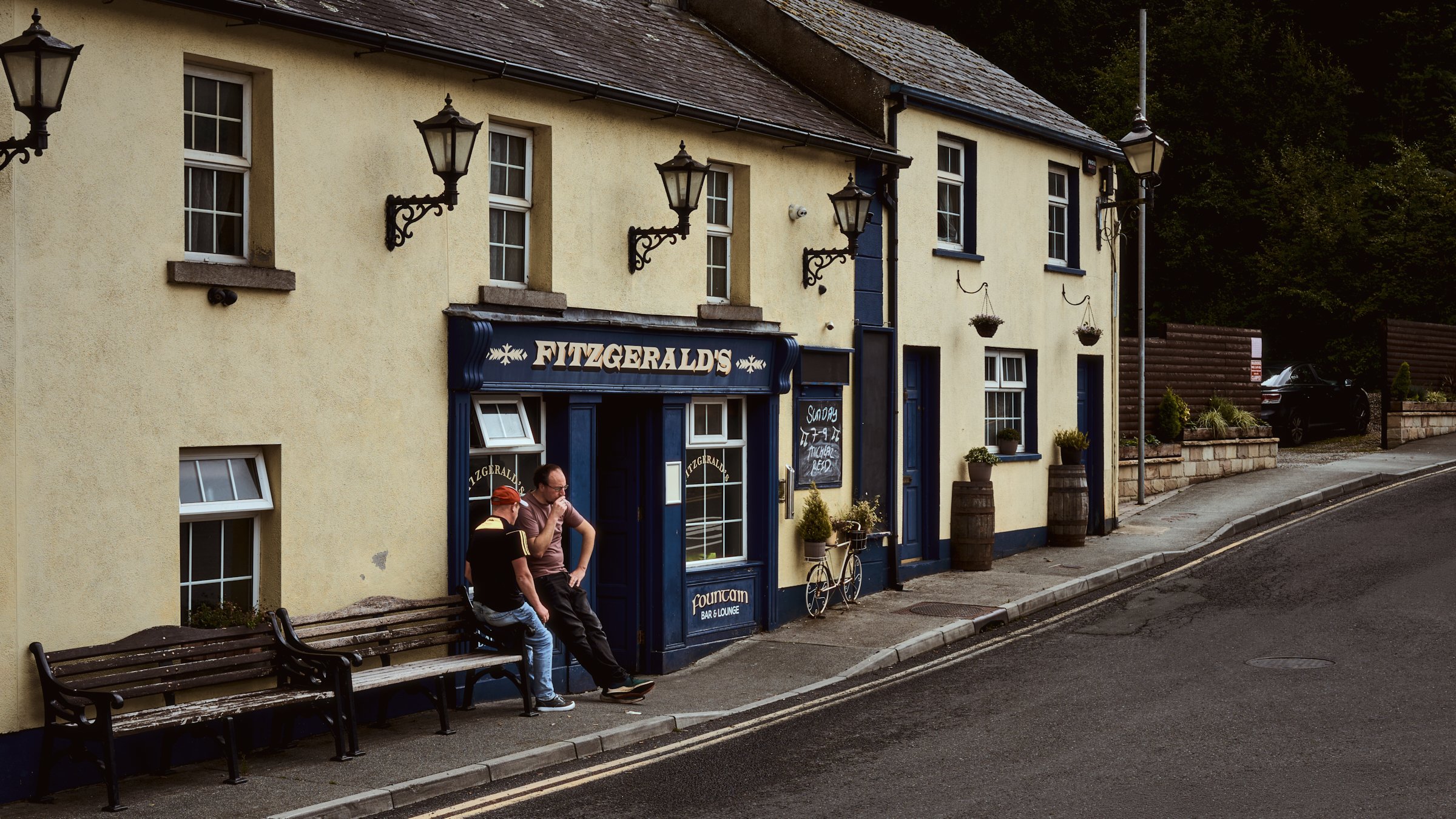 One Take - Ireland "Between Pints", Fitzgerald's, Avoca, Co Wicklow, Ireland 2024. A cinematic color photograph of two lads outside Fitzgerald's Pub smoking a cigarette. This pub was featured in the television show "Ballykissangel".