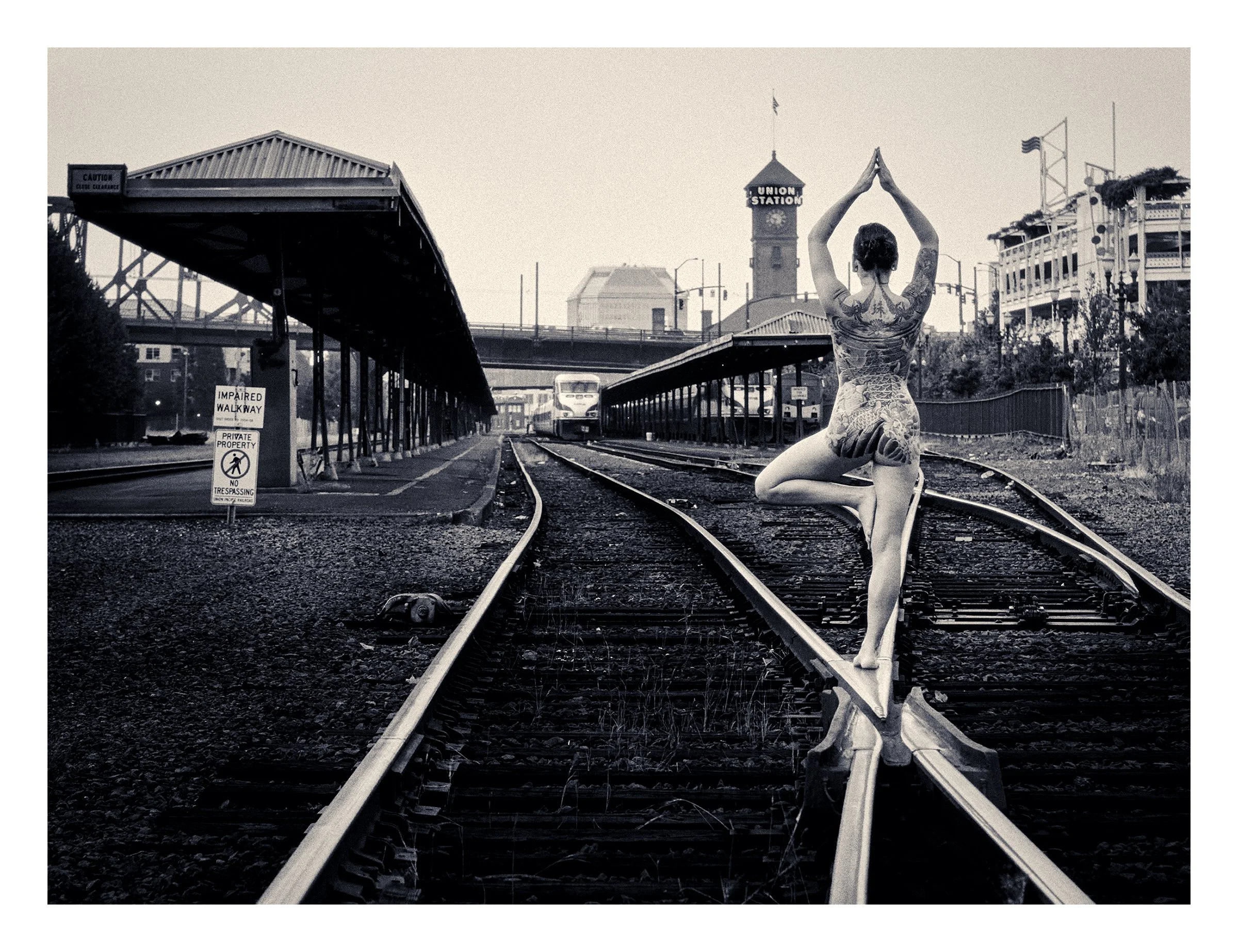 Bridgetown Nudes, MidnightMagenta, Union Station, Portland, Oregon, USA 2015 photographed by Dave Haworth. Monochrome picture of nude woman from the back in a yoga pose on train tracks in front of Union Station.