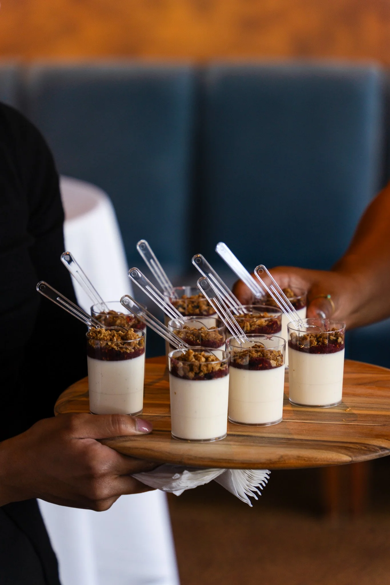 Tray of seven dessert parfaits with cream, berry topping, and crumble, each with a clear plastic spoon, taken at a catered community gathering and event in San Francisco. 