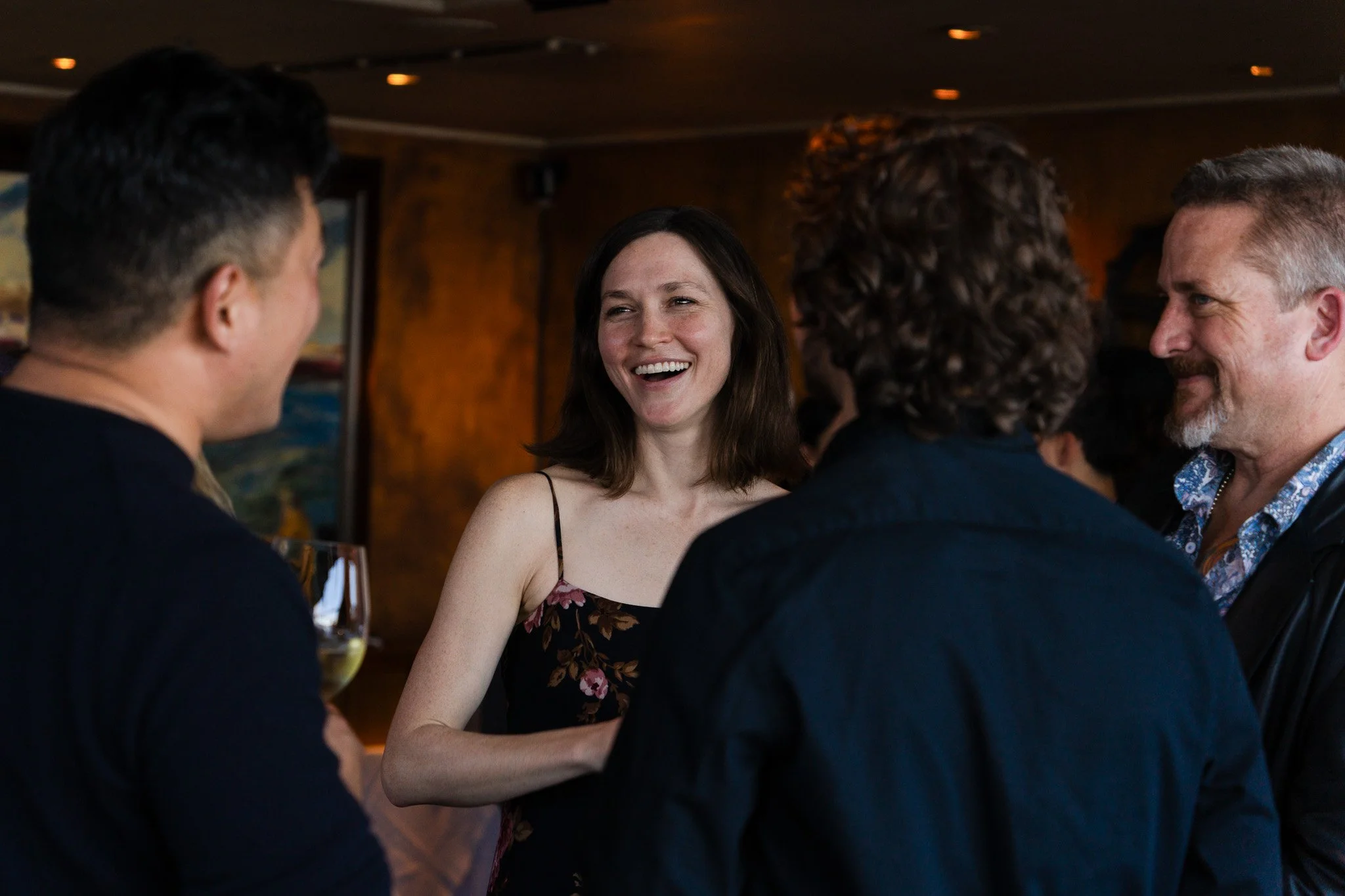 A group of people laughing and talking at a social gathering in a dimly lit indoor setting in San Francisco.