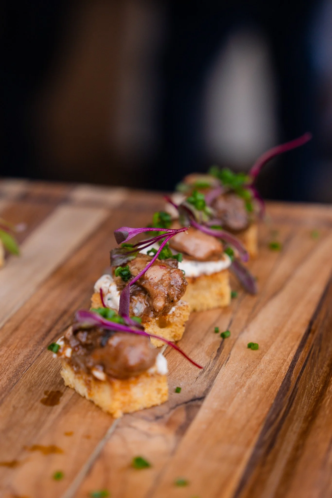 Small appetizers with meat, microgreens, and sauce on a wooden serving board at a community event in San Francisco.