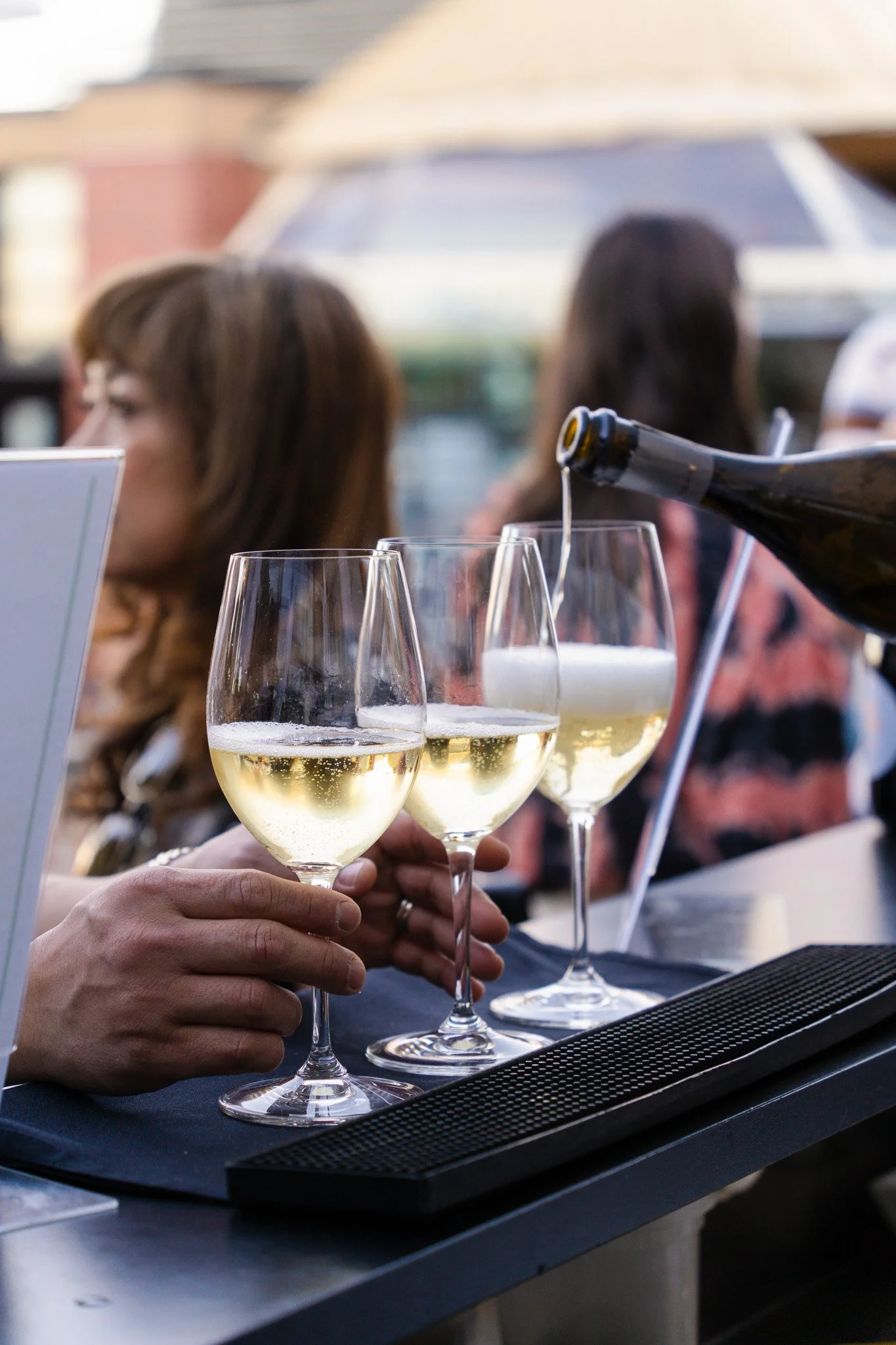 A person pouring champagne into glasses at an outdoor gathering in San Francisco, with a group of people socializing in the background.