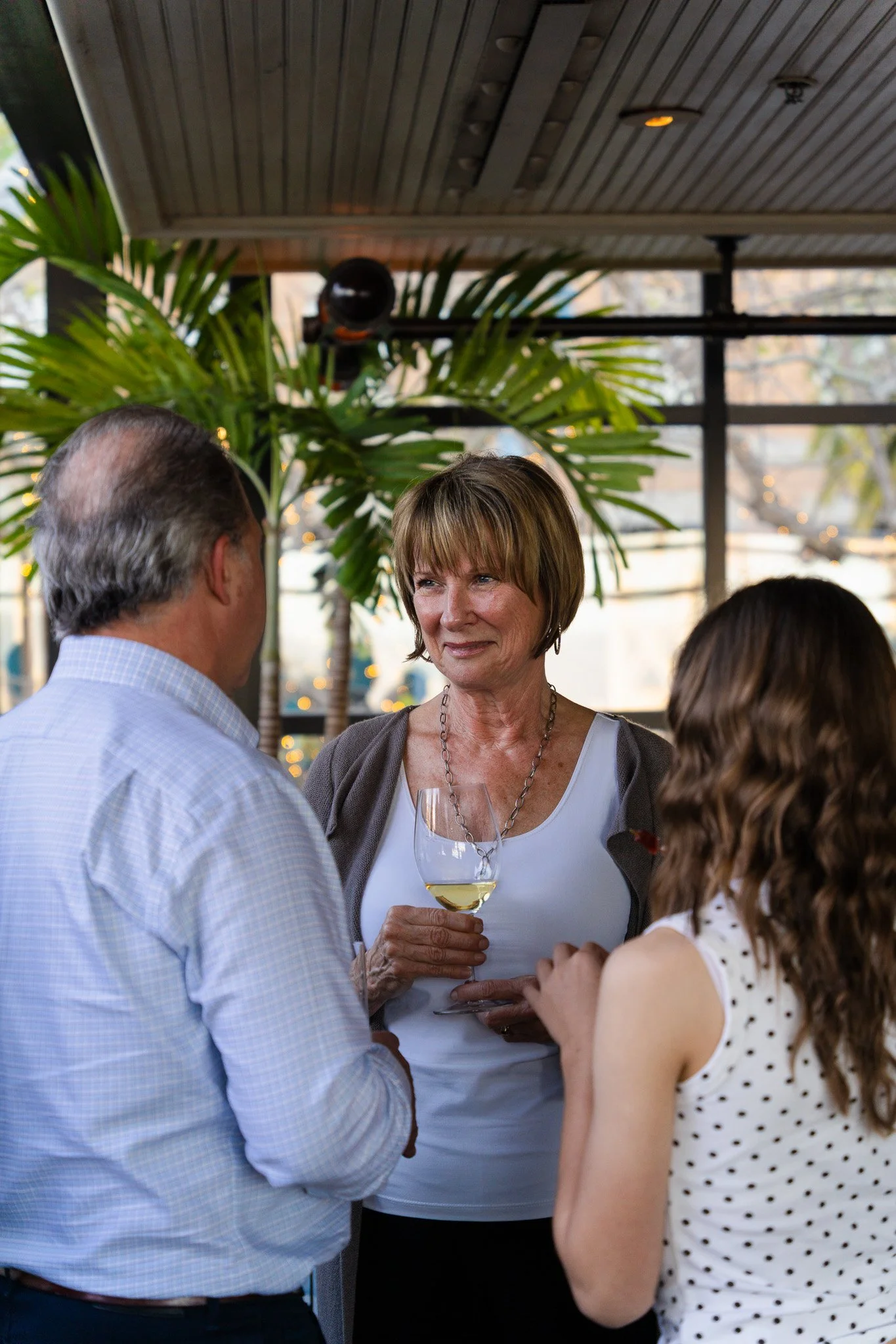 Three people, two women and one man, are having a conversation at a social gathering in San Francisco, with one woman holding a glass of white wine.